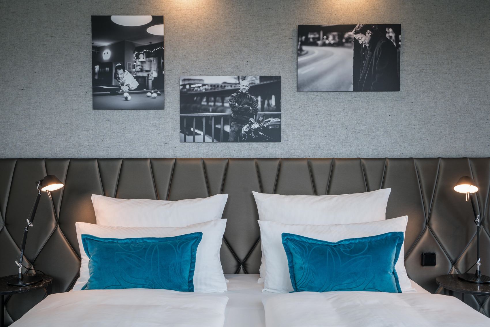 Designhotel Berlin Upper West Motel One Blick auf ein großes Doppelbett mit weißen Bezügen und Zierkissen in türkis sowie drei Gemälde an der Wand