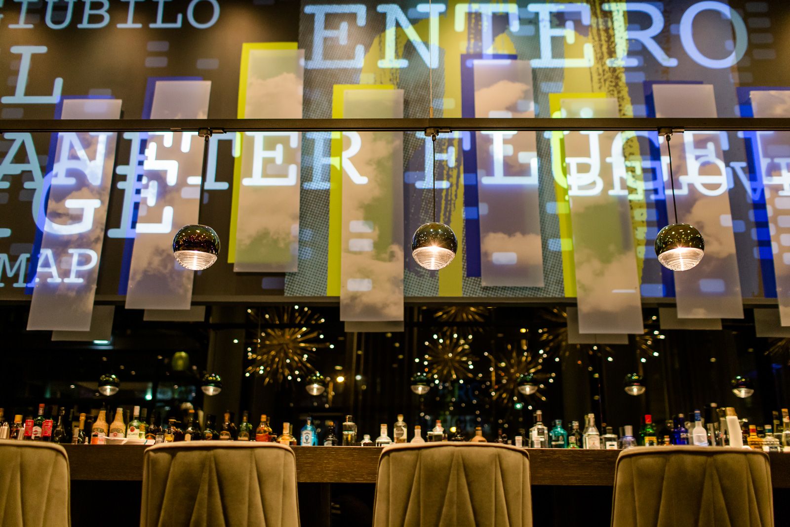 Hotel Bonn Beethoven Motel One lange Bar mit Lichtinstallation an der Wand sowie Spirituosen und Barhocker an der Theke