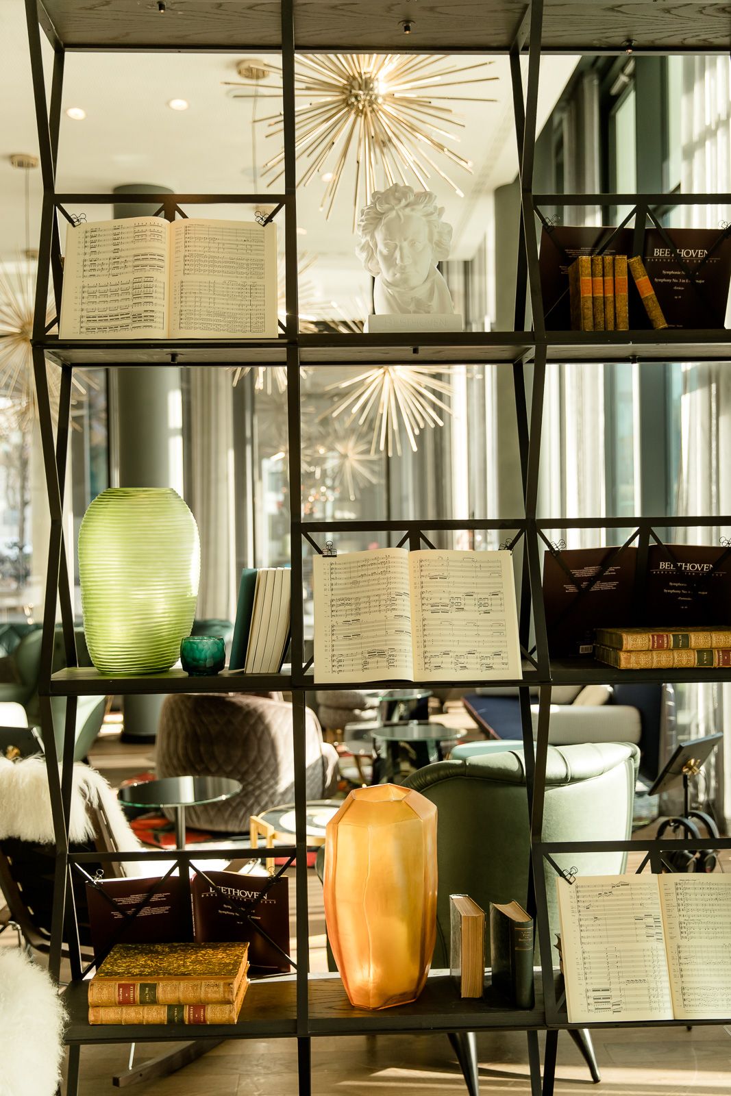 Hotel Bonn Beethoven Motel One offenes großes Regal mit viel Dekorationselementen und im Hintergrund der Blick in die helle Lounge