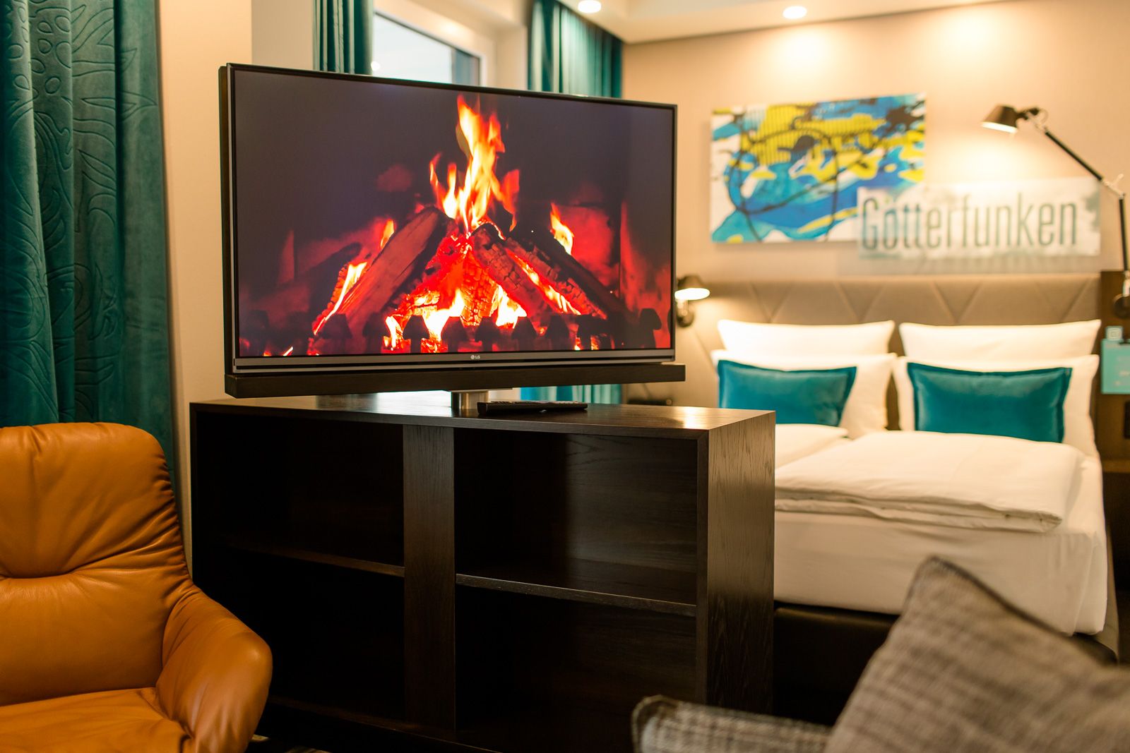 Hotel Bonn Beethoven Motel One Zimmer mit Blick auf einen Fernseher auf einer offenen Kommode sowie ein Sessel daneben und ein Doppelbett im Hintergrund