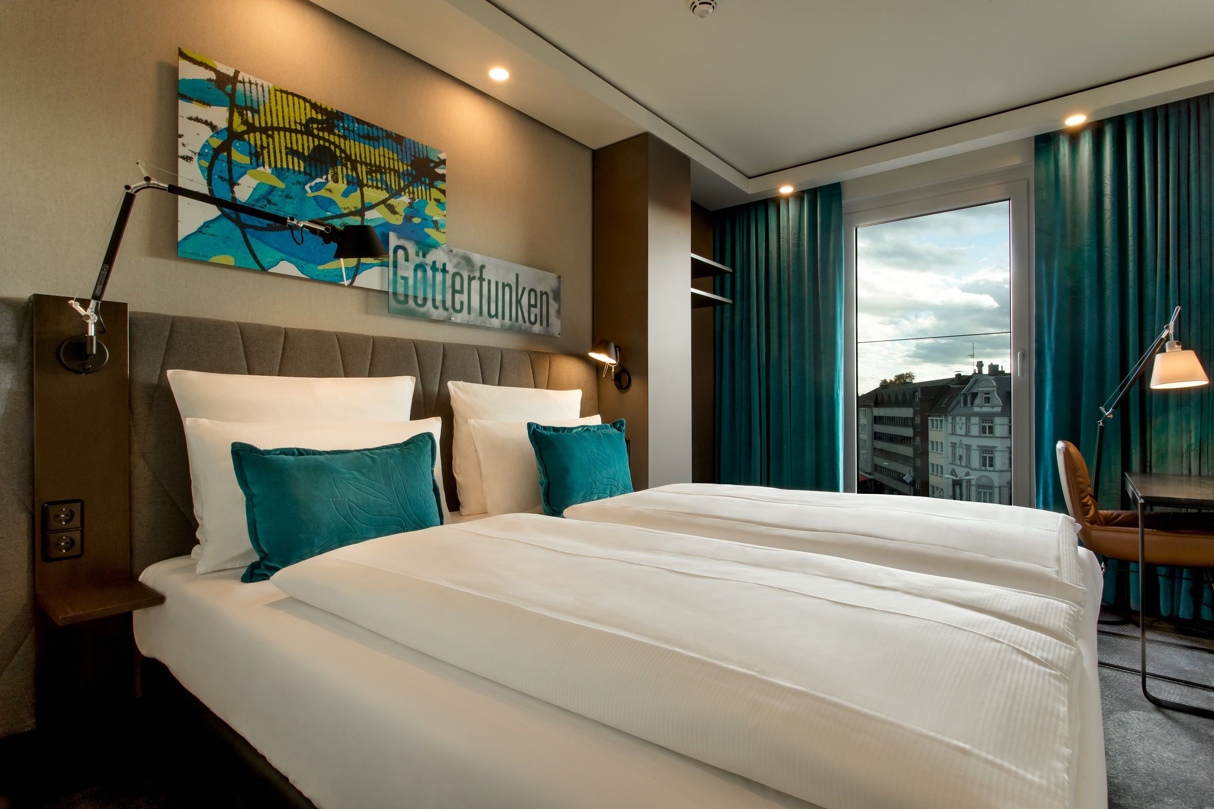 hotel Bonn Beethoven Motel One view of a bright room with a double bed and a table and chair in front of a floor-to-ceiling window