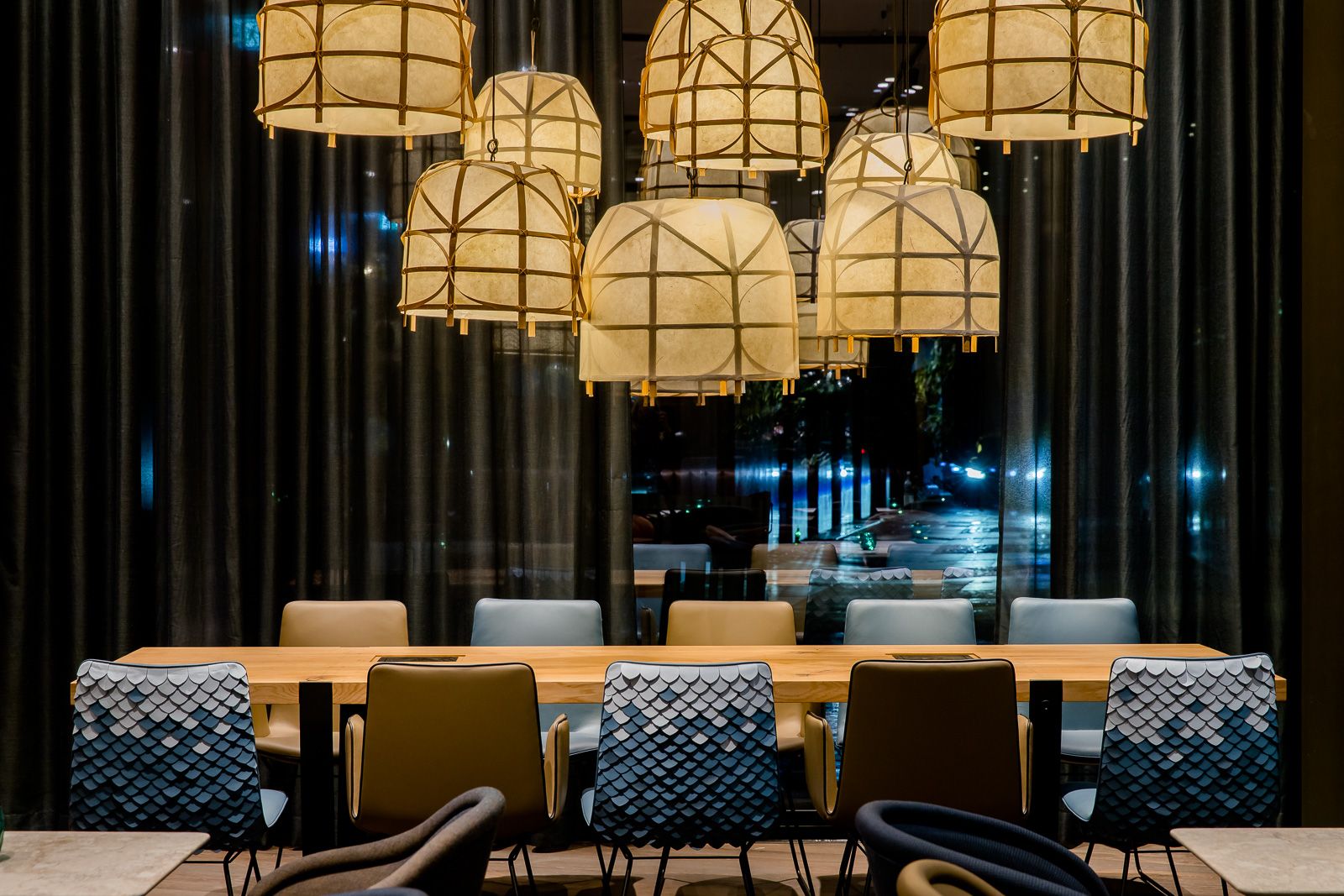 Hotel Bonn Hauptbahnhof Motel One Lounge bei Abend mit langem Tisch und mehreren Stühlen sowie bodentiefen Fenstern mit Blick nach draußen