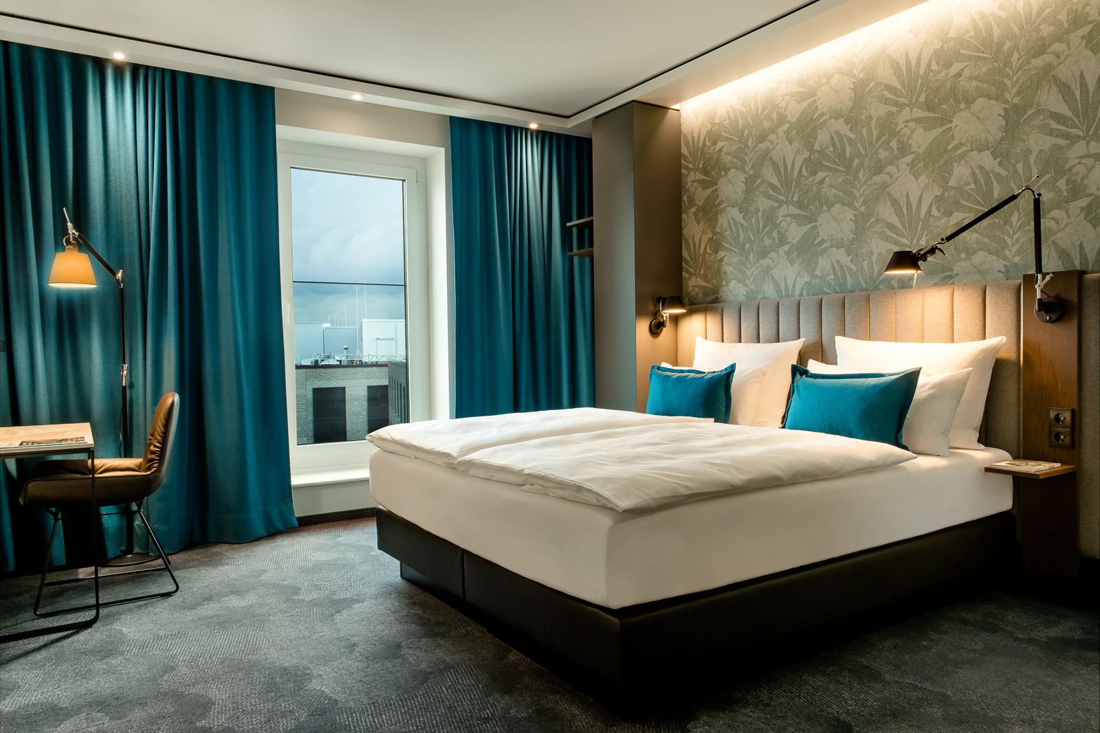 Hotel Bonn Hauptbahnhof Motel One großes und helles Zimmer mit Doppelbett, Tisch und Stuhl sowie bodentiefes Fenster