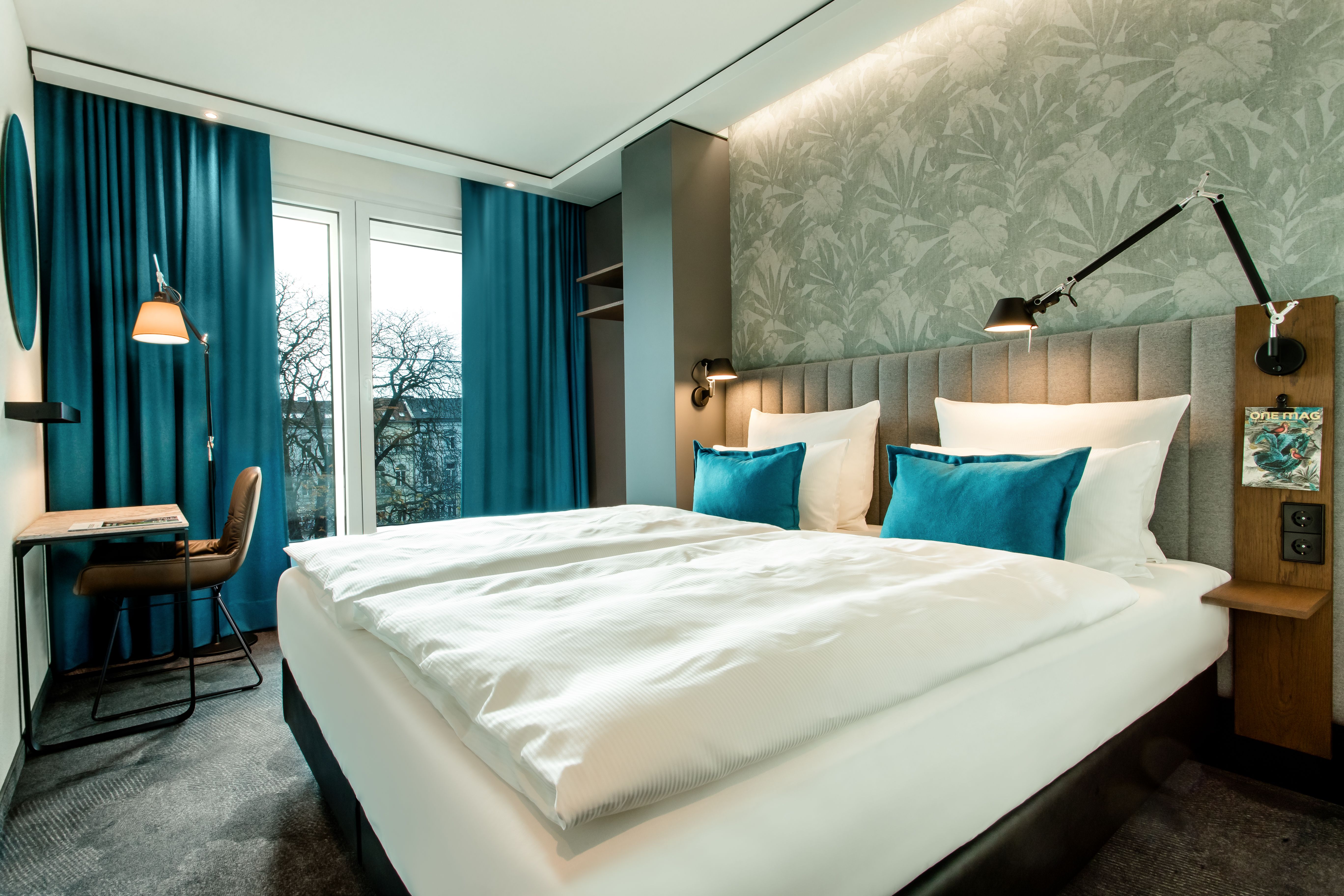 Hotel Bonn Hauptbahnhof Motel One lichtdurchflutetes Doppelzimmer mit großem Bett, Tisch, Stuhl und bodentiefem Fenster