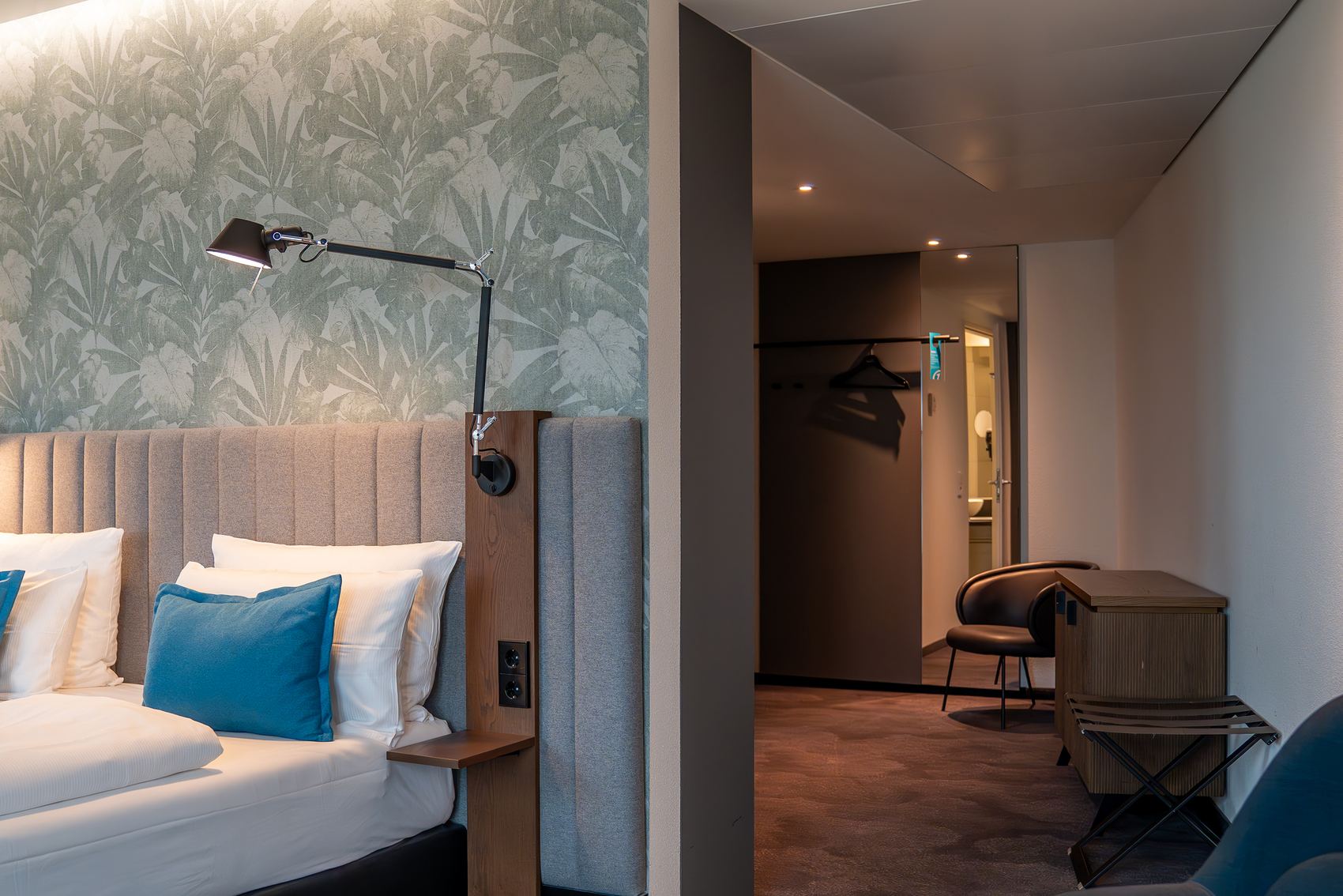 Hotel Bonn Hauptbahnhof Motel One großes Zimmer mit Blick auf ein Doppelbett sowie in einen großen Flur mit Kommode, Sessel und Garderobe