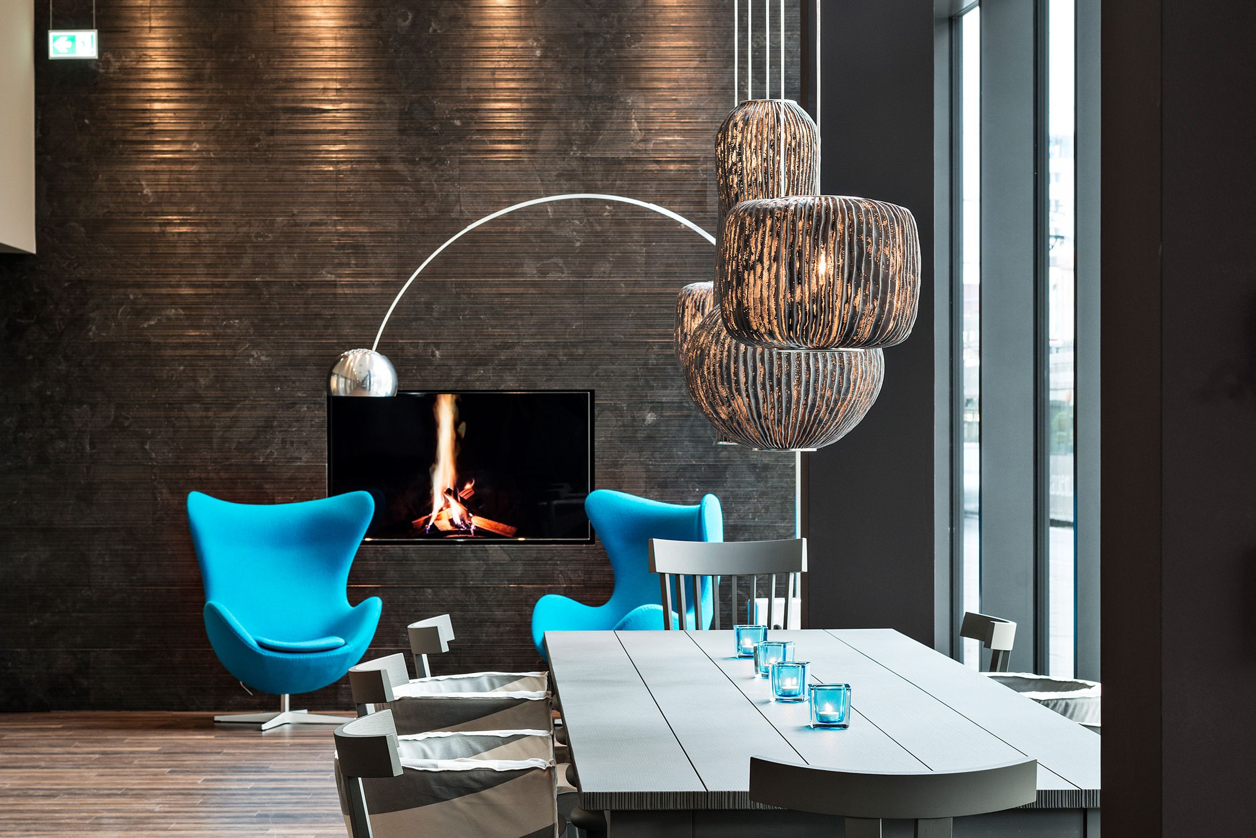 designhotel Bremen Motel One bright lounge with a long table and two egg chairs in the background with a TV on the wall