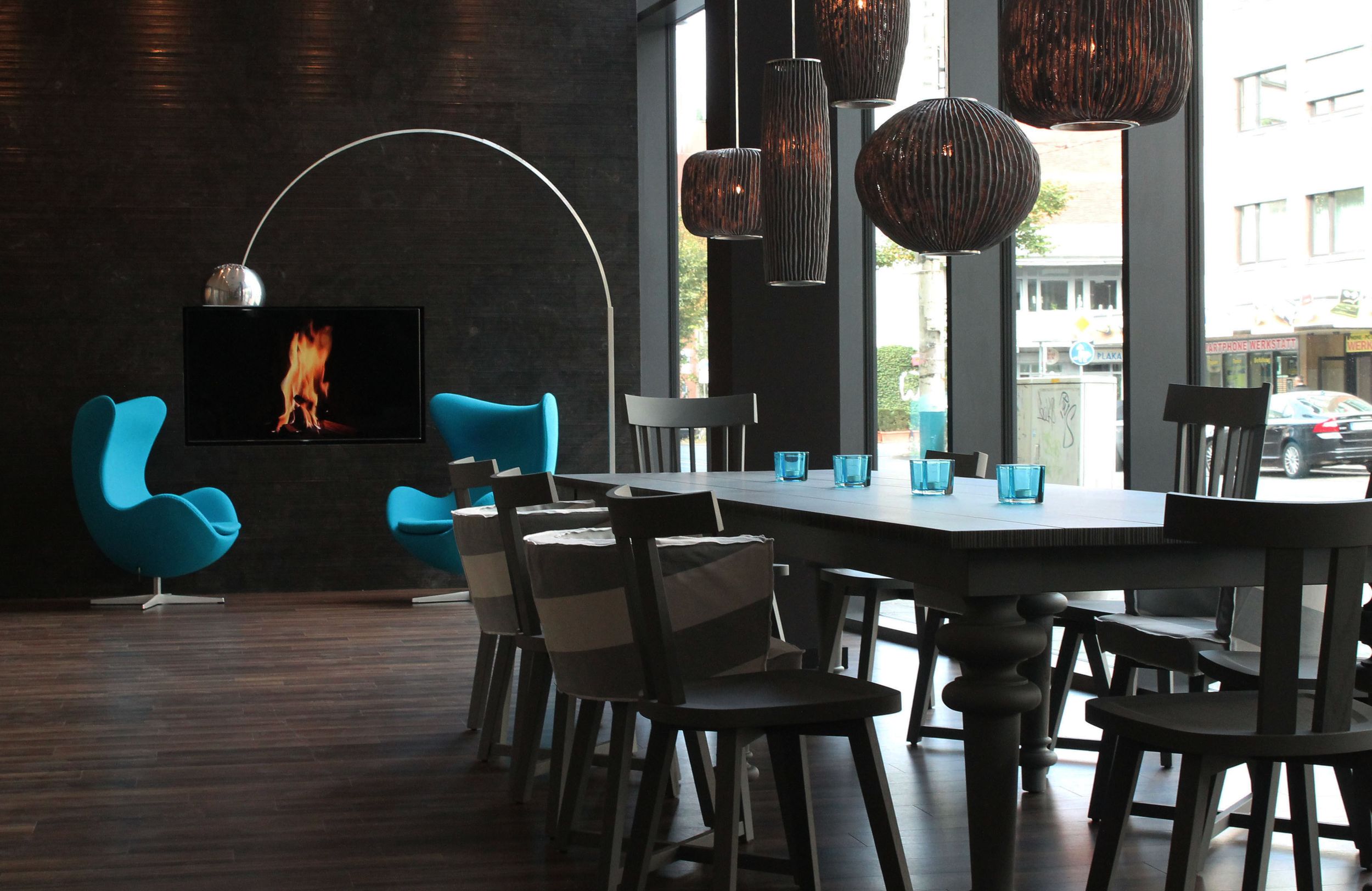 Designhotel Bremen Motel One Lounge mit großer Fensterfront sowie langem Tisch und zwei Egg Chairs im Hintergrund