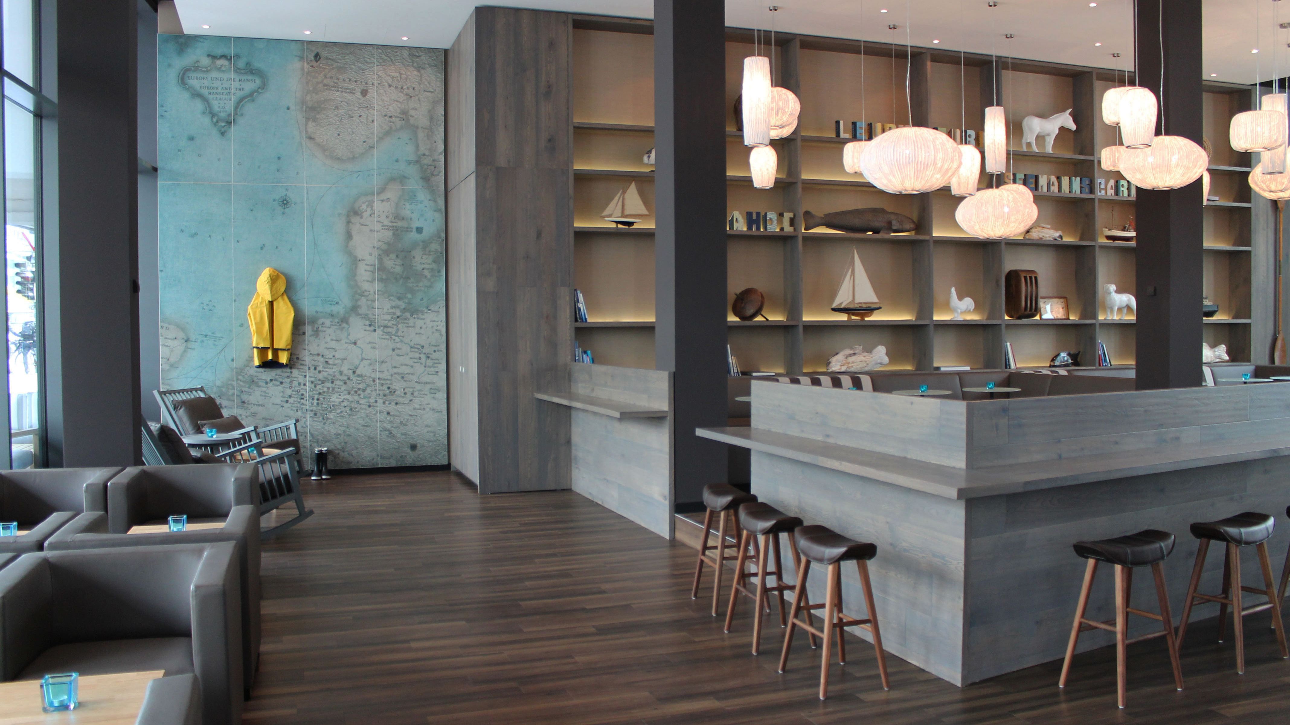 Hotel Bremen Motel One helle Lounge mit mehreren Sitzgelegeneheiten sowie einer großen Wand mit Weltkarte und gelbem Regenmantel