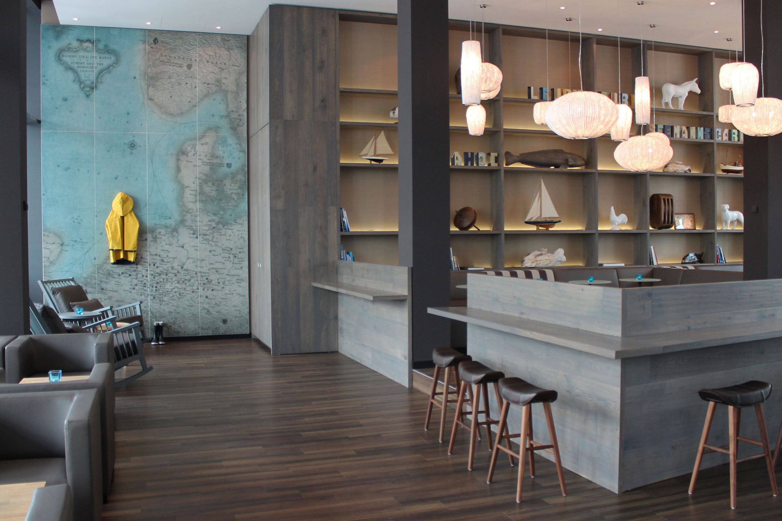 hotel Bremen Motel One bright lounge with several seating areas and a large wall with a world map and yellow raincoat