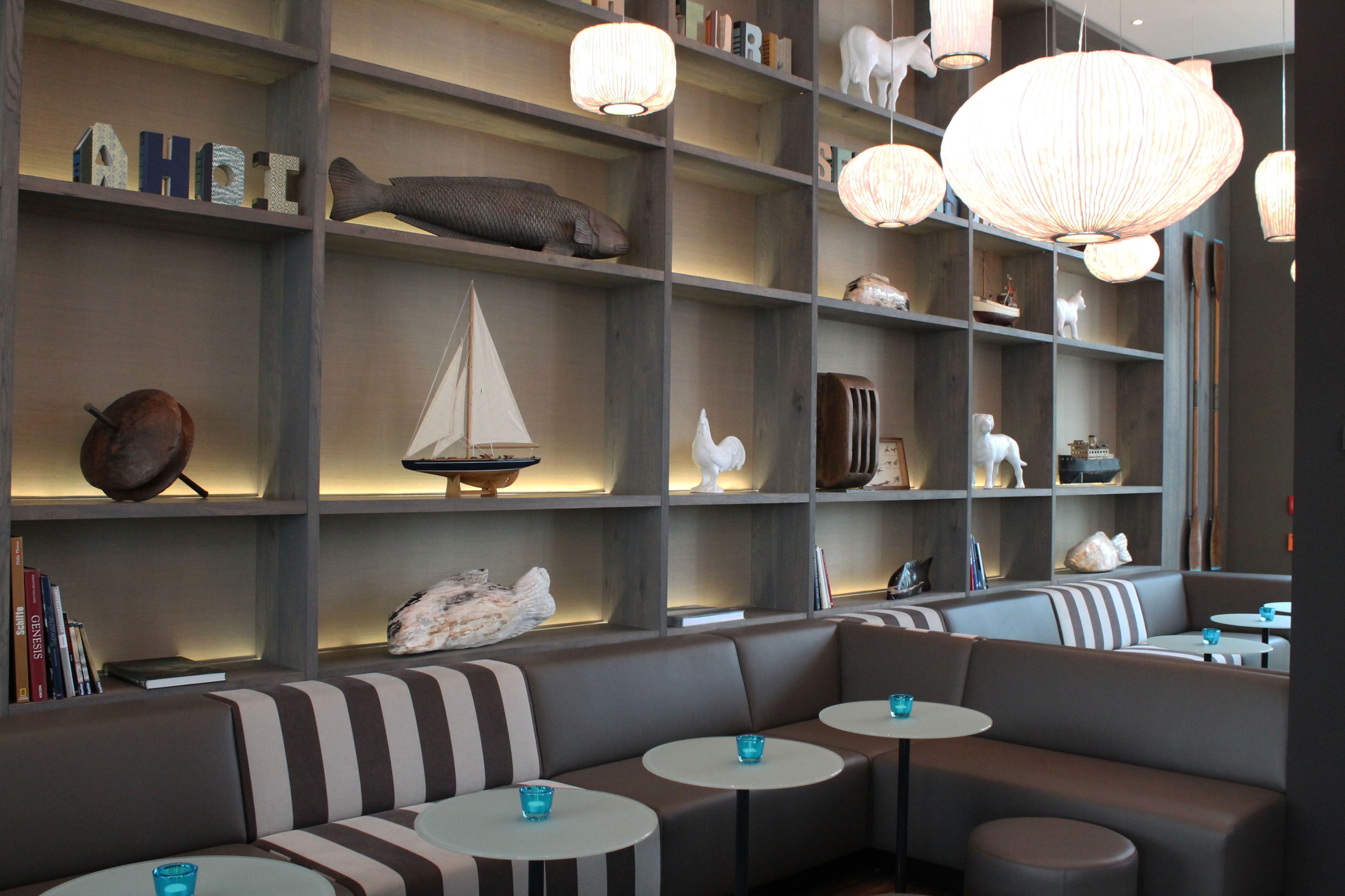 Hotel Bremen Motel One helle Lounge mit mehreren Sitzgelegenheiten vor einem großen Regal mit Dekoration in einzelnen Fächern