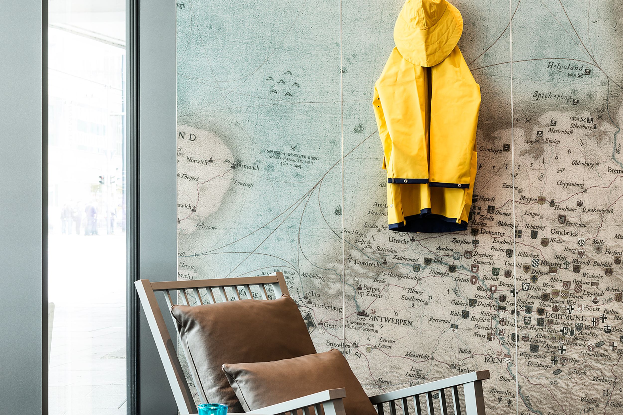 designhotel Bremen Motel One bright lounge with two chairs and a side table in front of a wall with a world map and a yellow rain jacket