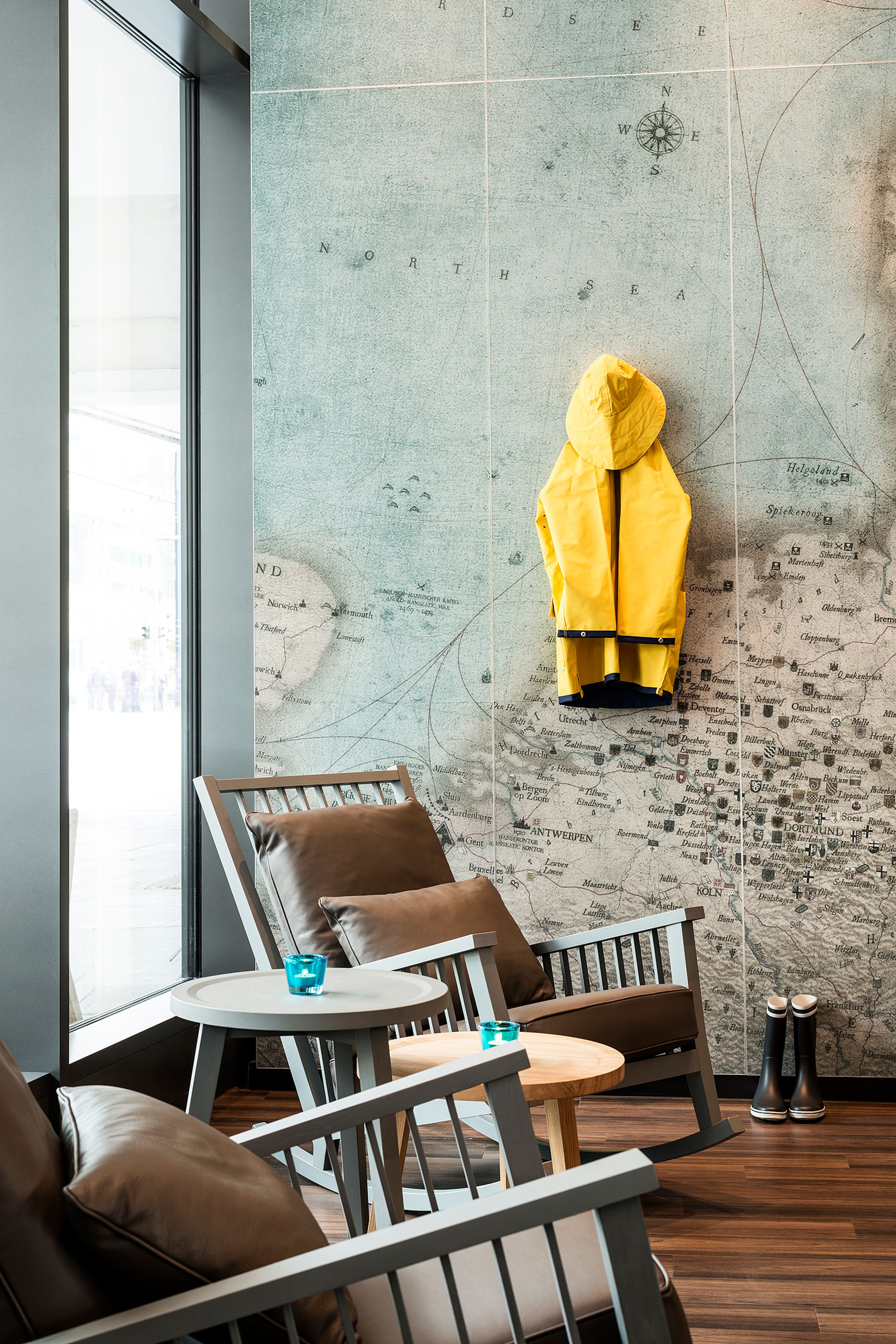 Designhotel Bremen Motel One helle Lounge mit zwei Stühlen und Beistelltisch vor einer Wand mit Weltkarte und gelber Regenjacke