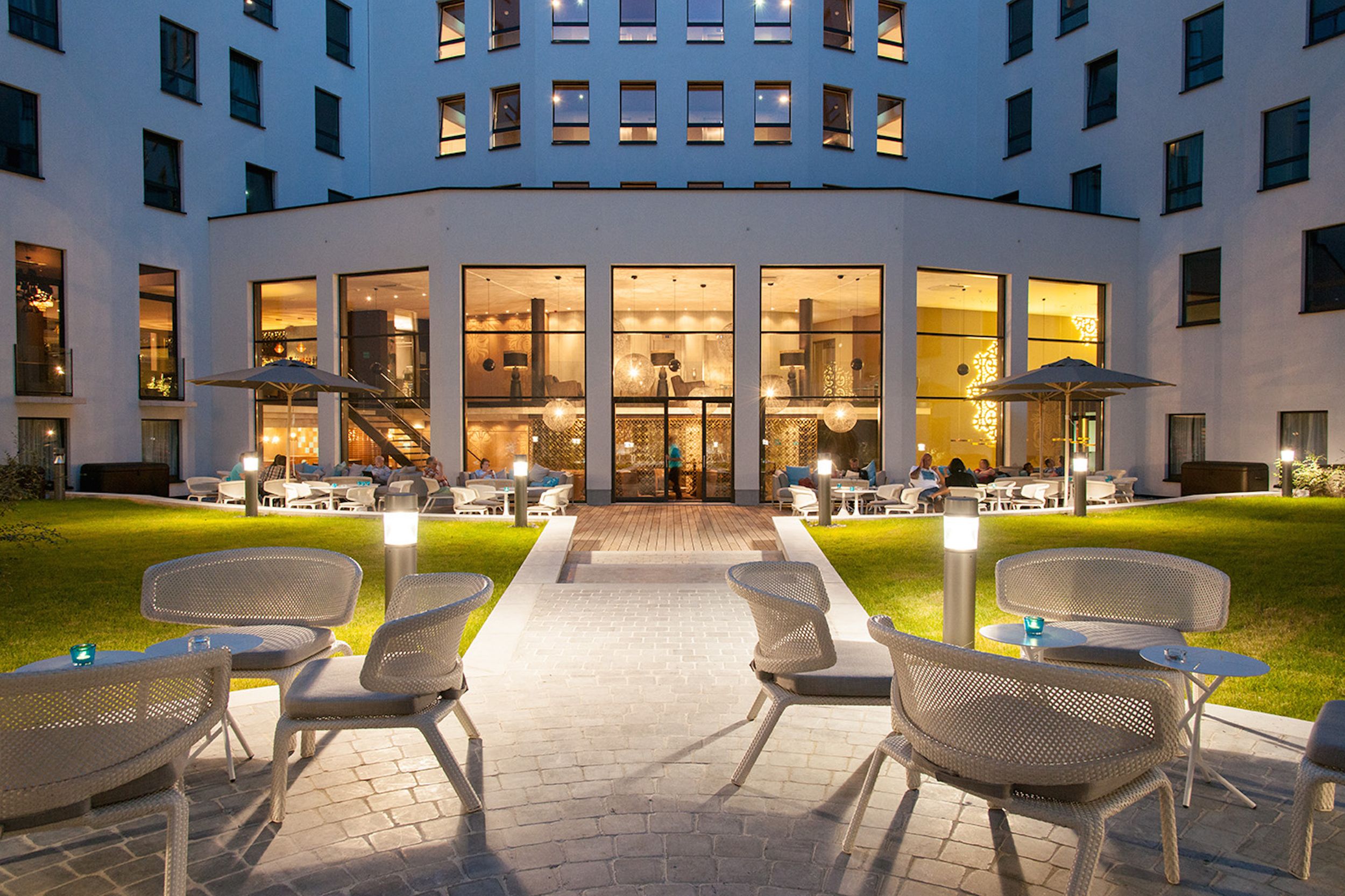 Designhotel Brüssel Motel One Außenbereich bei Abend mit Sitzgelegenheiten und Blick auf das Gebäude