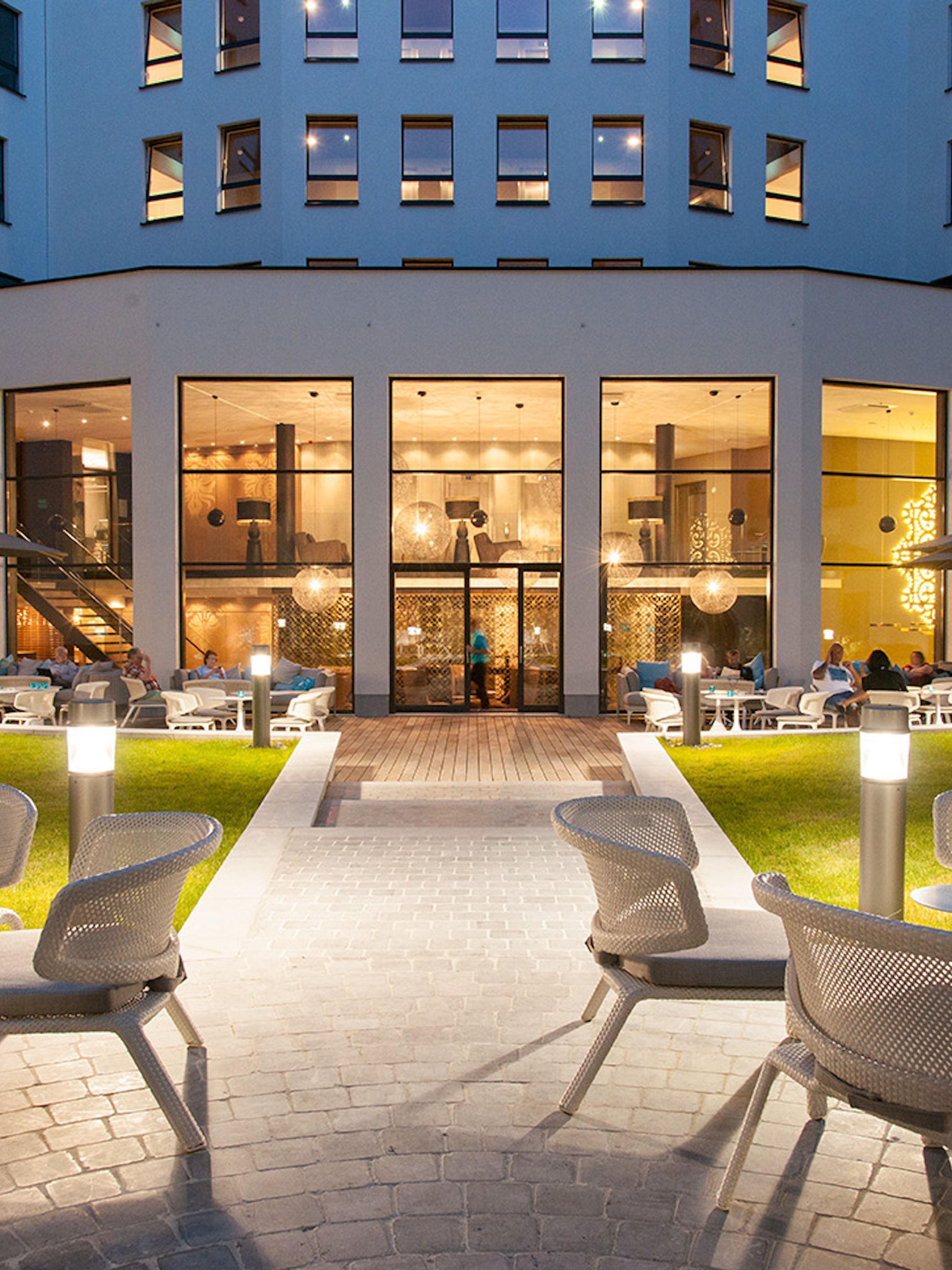 Designhotel Brüssel Motel One Außenbereich bei Abend mit Sitzgelegenheiten und Blick auf das Gebäude