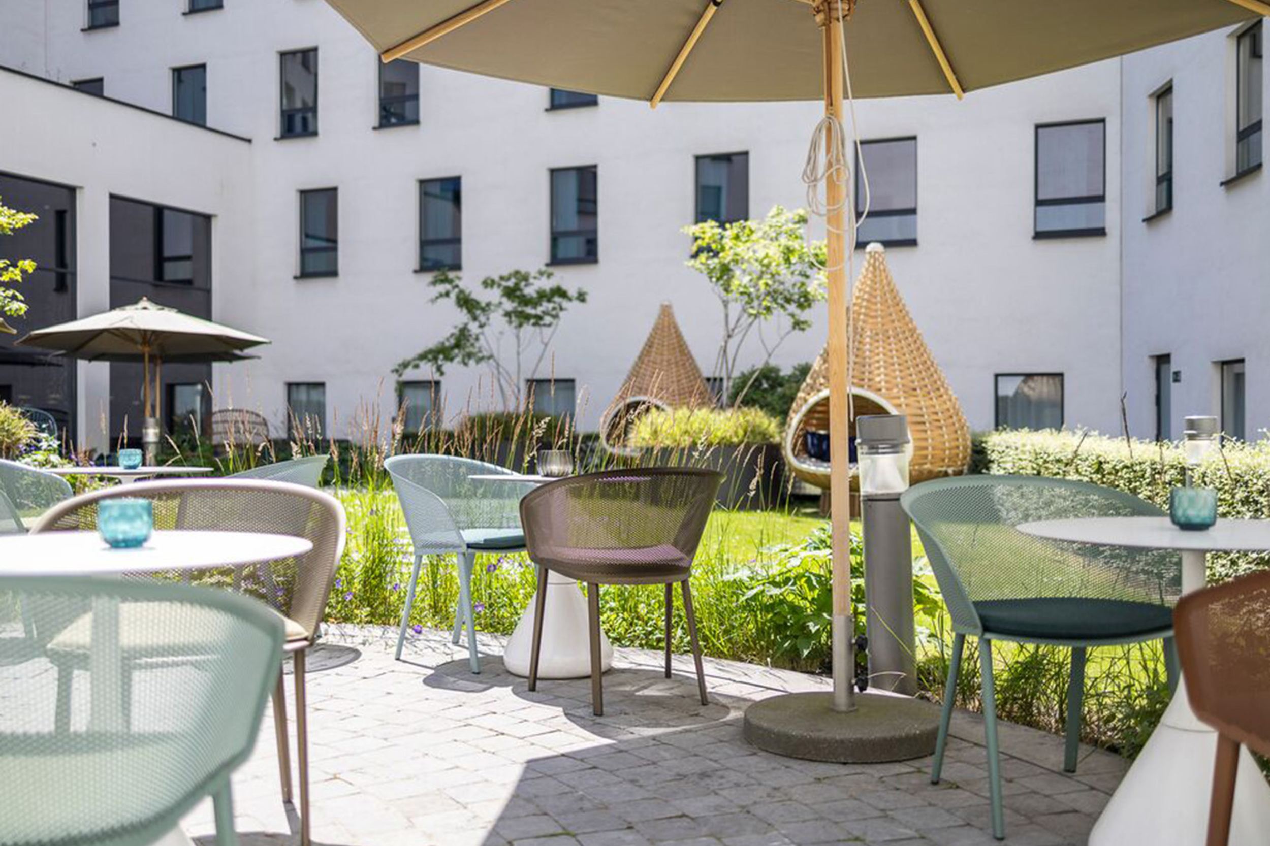 Designhotel Brüssel Motel One Terrasse mit Sonnenschein, vielen Tischen und Stühlen sowie ein großer Sonnenschirm