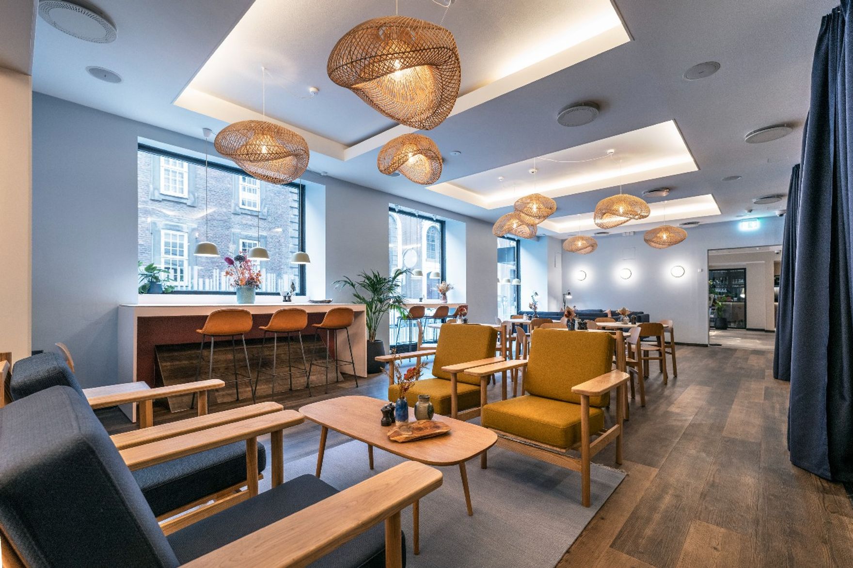 Hotel Kopenhagen Motel One heller Frühstücksraum mit mehreren Tischen und Stühlen sowie Hochtische vor großem Fenster