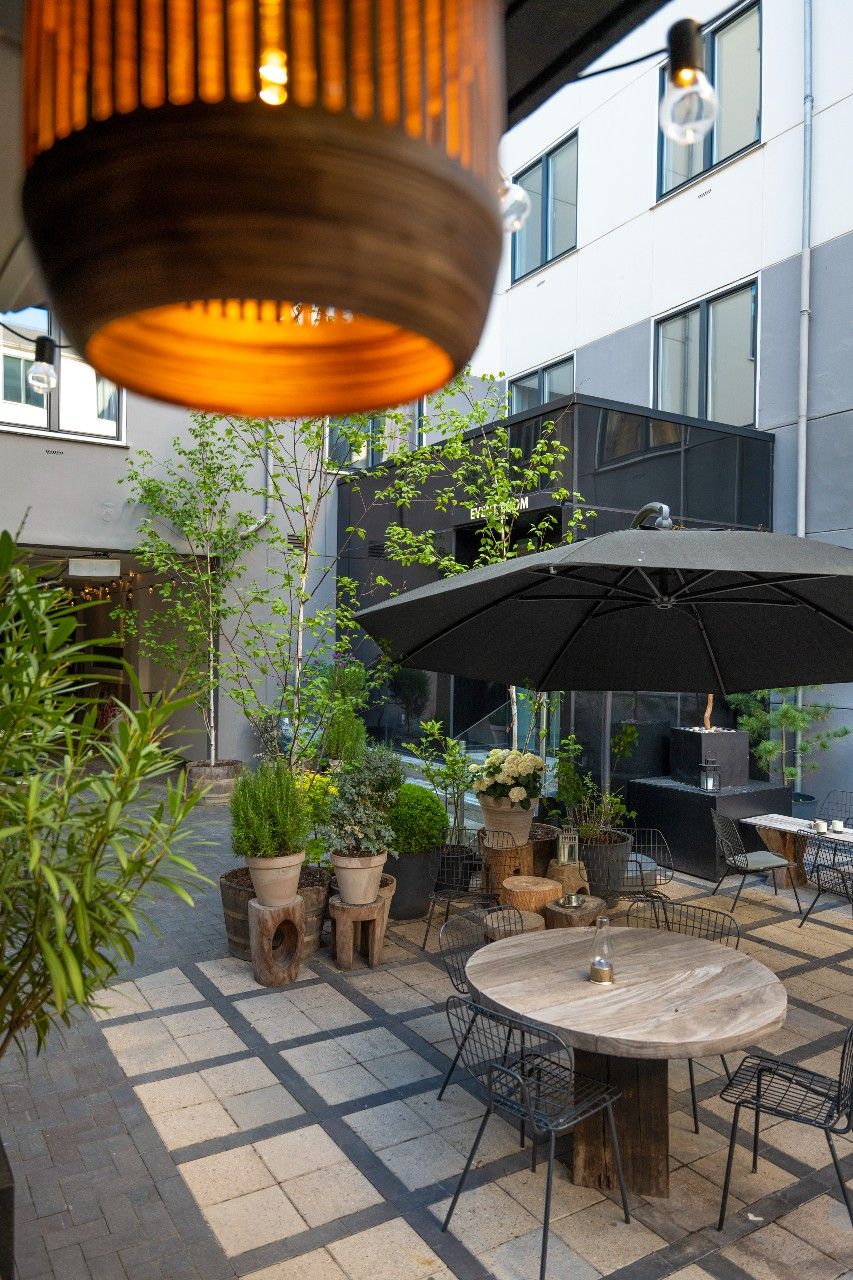 Designhotel Kopenhagen Motel One Innenhof mit mehreren Tischen und Stühlen sowie einem Sonnenschirm und großer Lampe