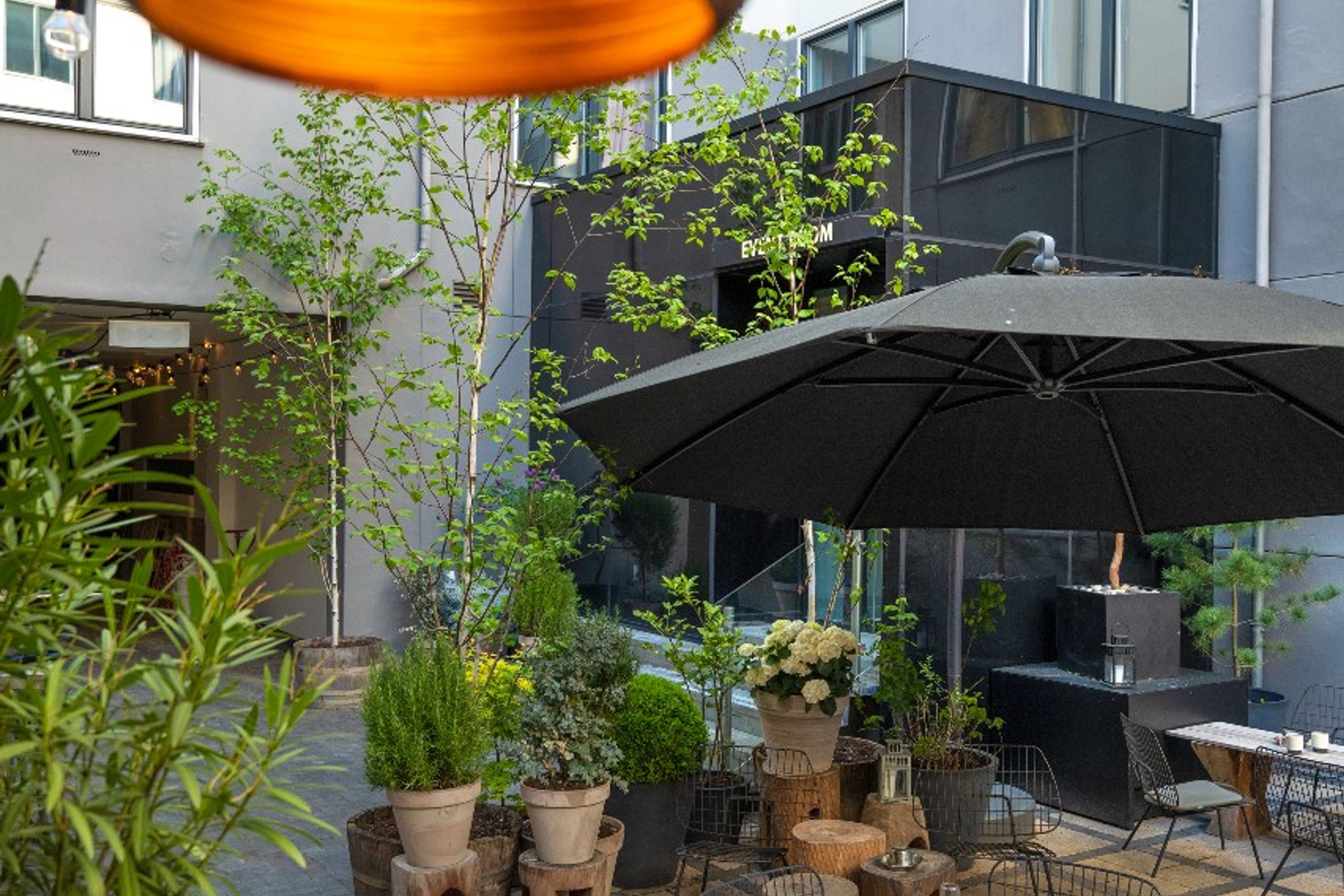 Designhotel Kopenhagen Motel One Innenhof mit mehreren Tischen und Stühlen sowie einem Sonnenschirm und großer Lampe