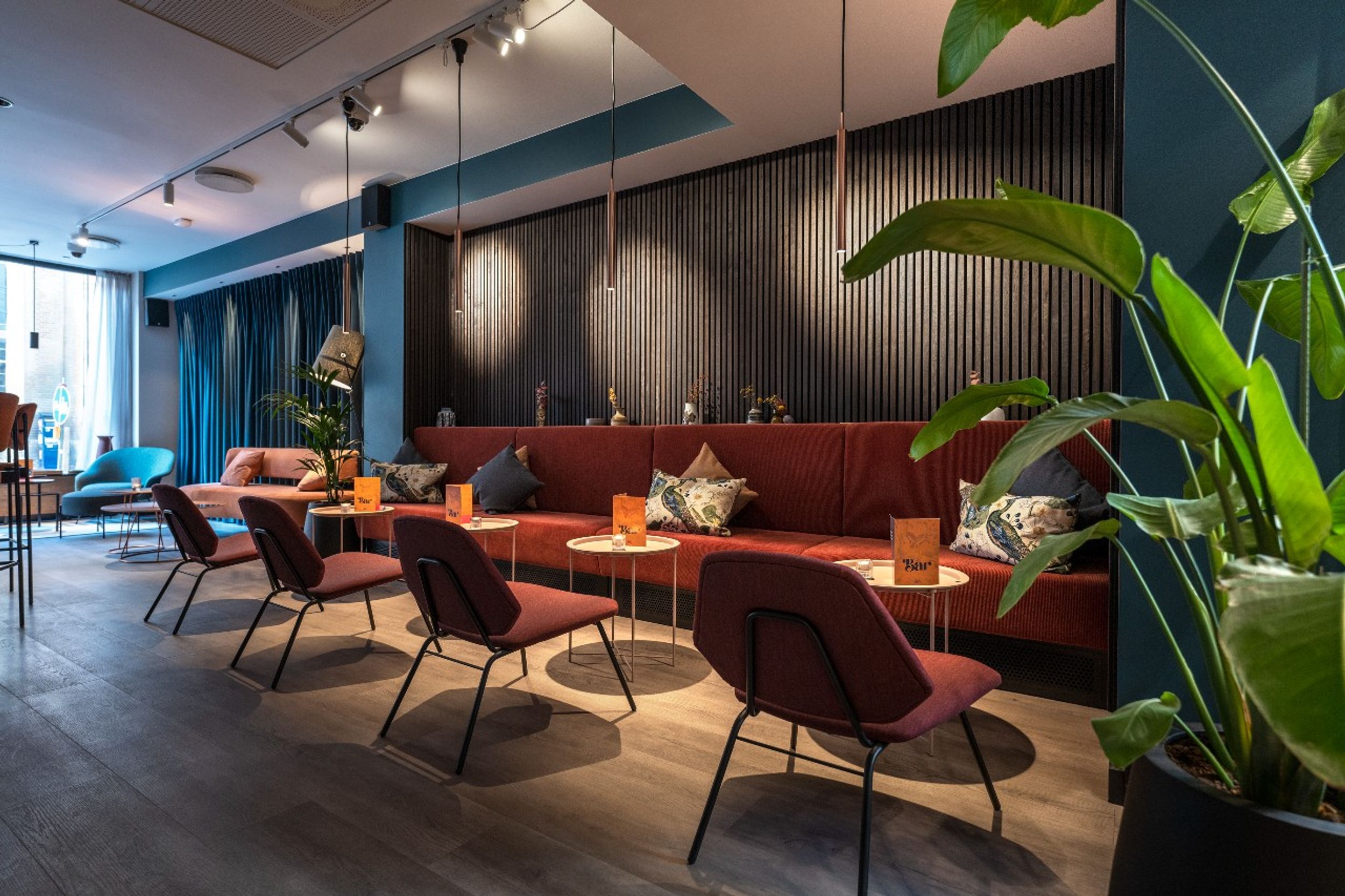 hotel Copenhagen Motel One light-filled lounge with a long bench and many dark red chairs for relaxing