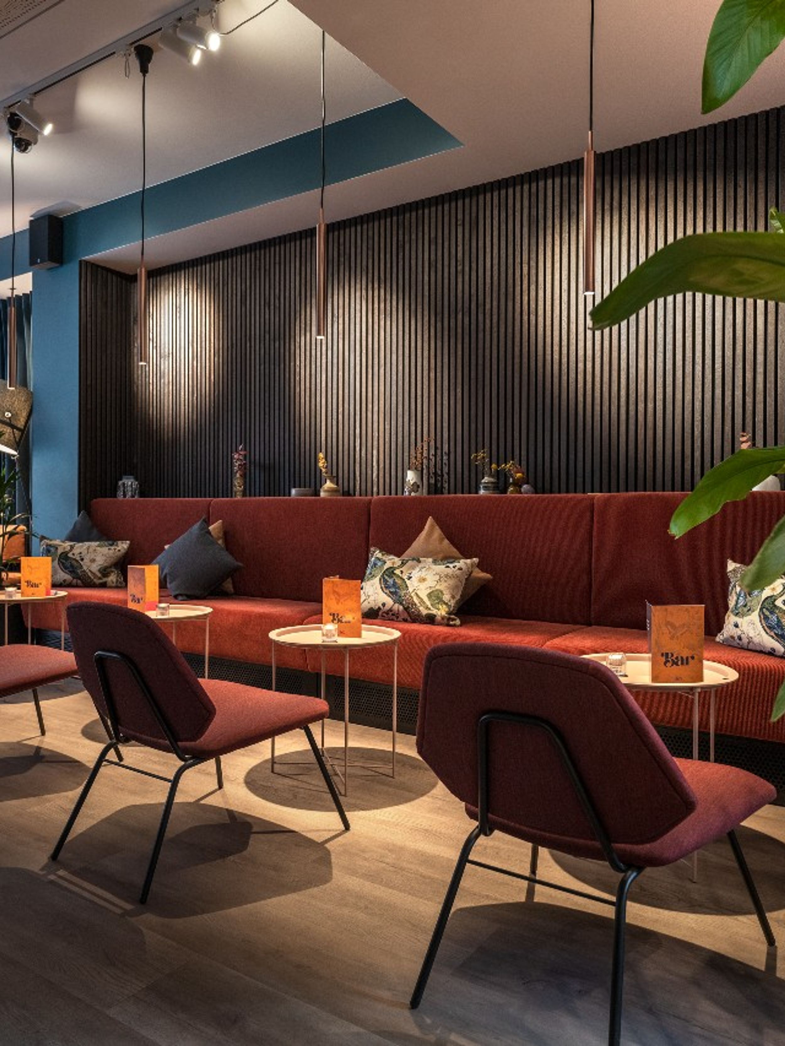 hotel Copenhagen Motel One light-filled lounge with a long bench and many dark red chairs for relaxing