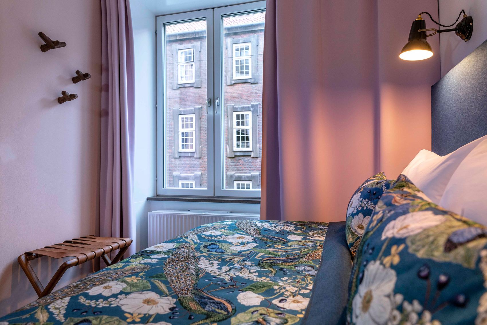 hotel Copenhagen Motel One side view across a large double bed to a pink wall and a window with light pink curtains