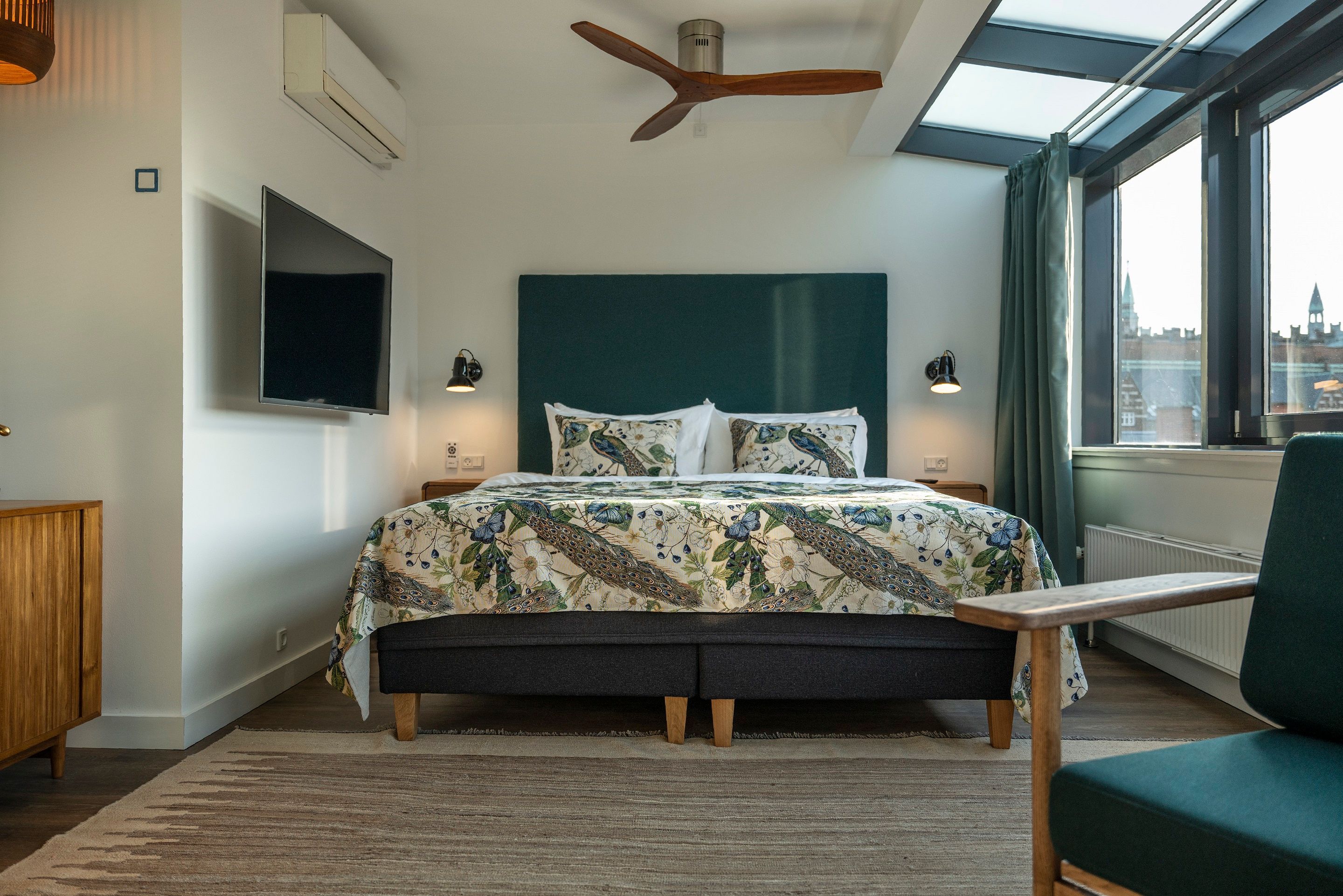 Hotel Kopenhagen Motel One Suite mit großem Doppelbett, Ventilator an der Decke, Fernseher an der Wand sowie ein Sessel im Vordergrund