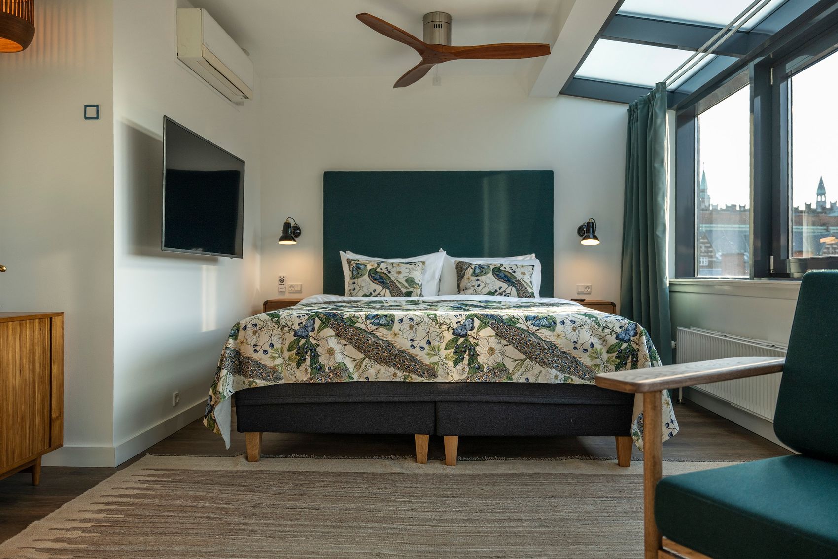 Hotel Kopenhagen Motel One Suite mit großem Doppelbett, Ventilator an der Decke, Fernseher an der Wand sowie ein Sessel im Vordergrund