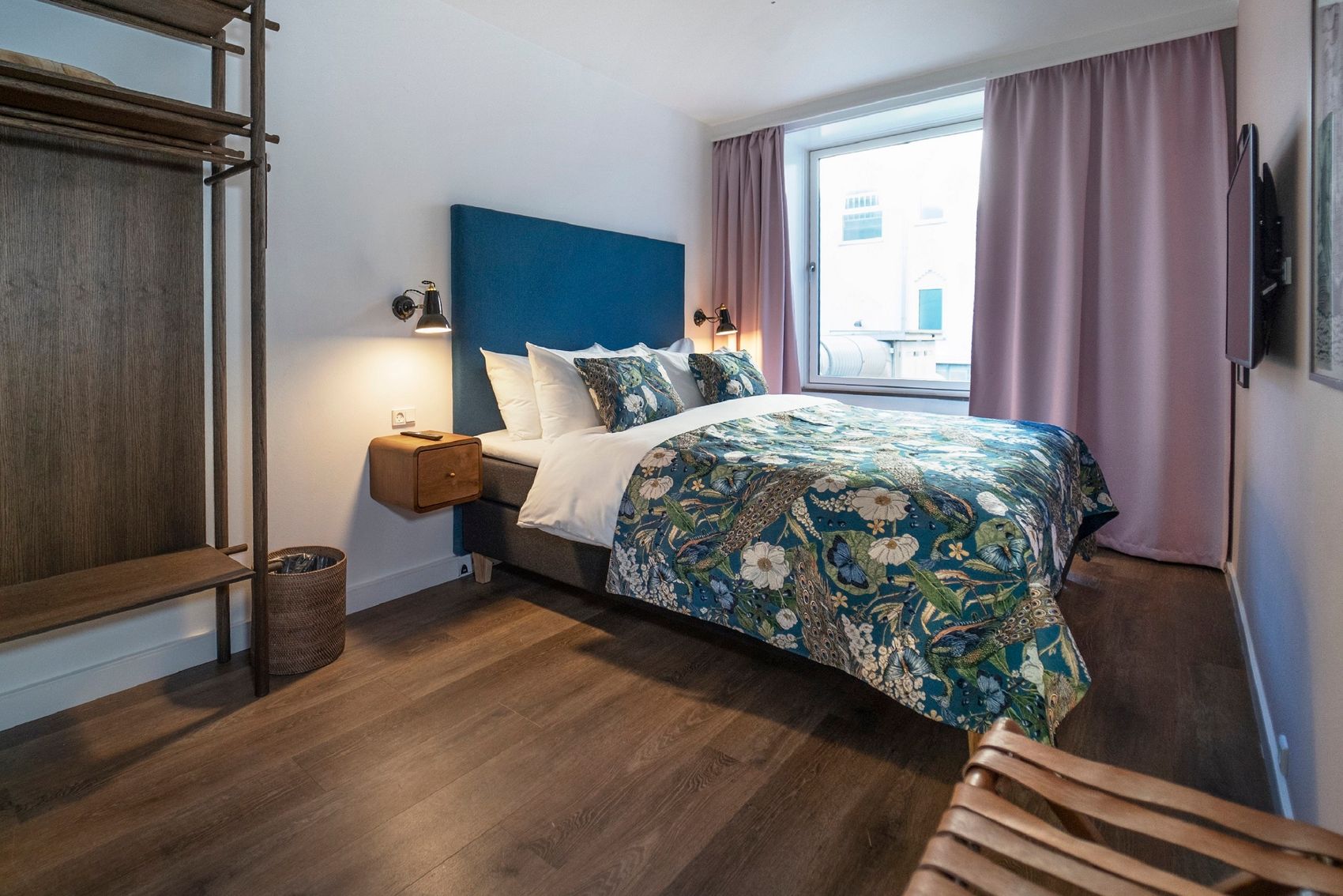 Designhotel Kopenhagen Motel One helles Doppelzimmer mit Bett, blauem Kopfteil, Vorhängen in rosa und offenem Kleiderschrank