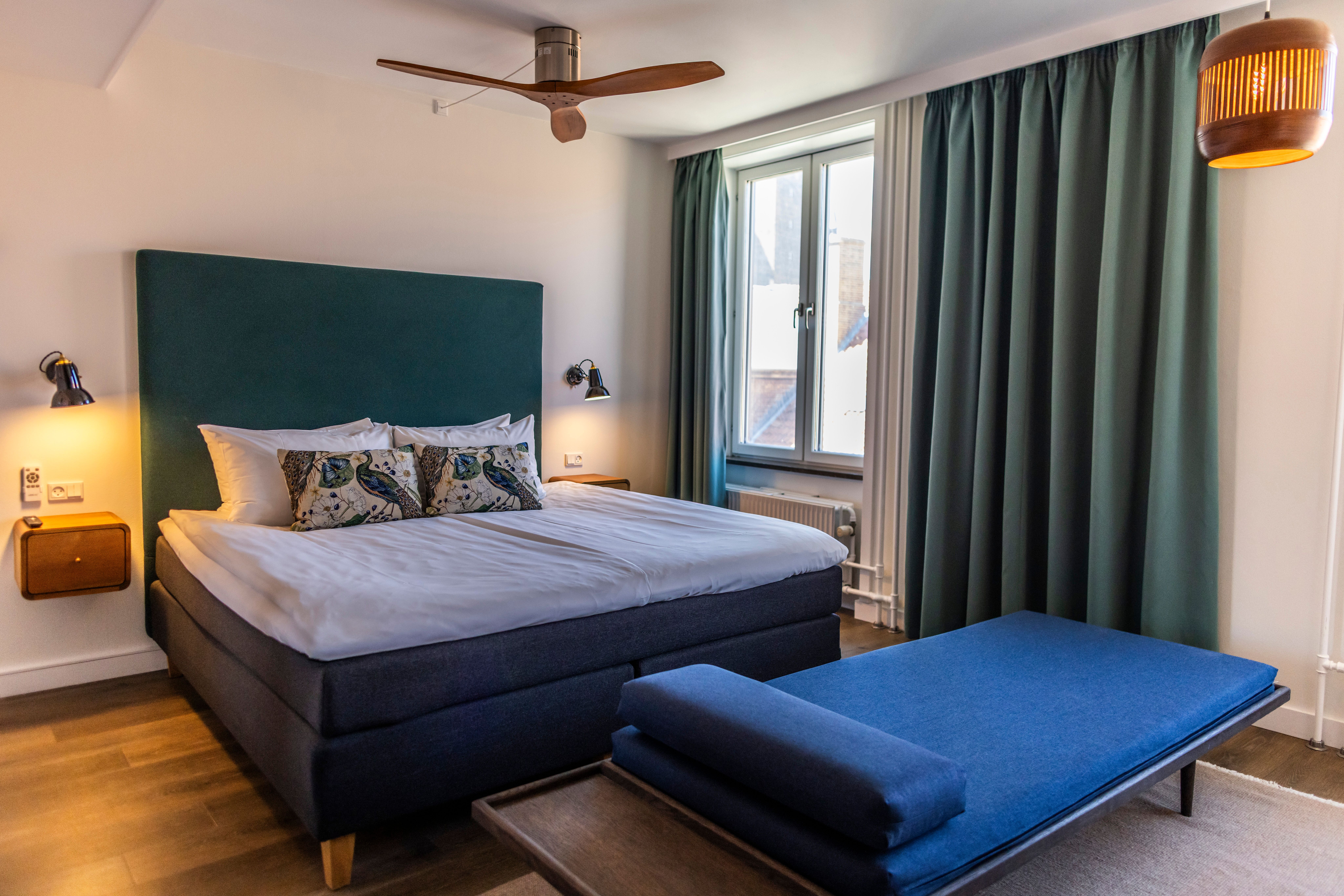 Hotel Motel One Copenhagen Modernes Hotelzimmer mit großem, komfortablem Doppelbett, weichen Kissen, großen Fenstern und ruhiger Atmosphäre durch gedämpfte Beleuchtung und dekorative Vorhänge.