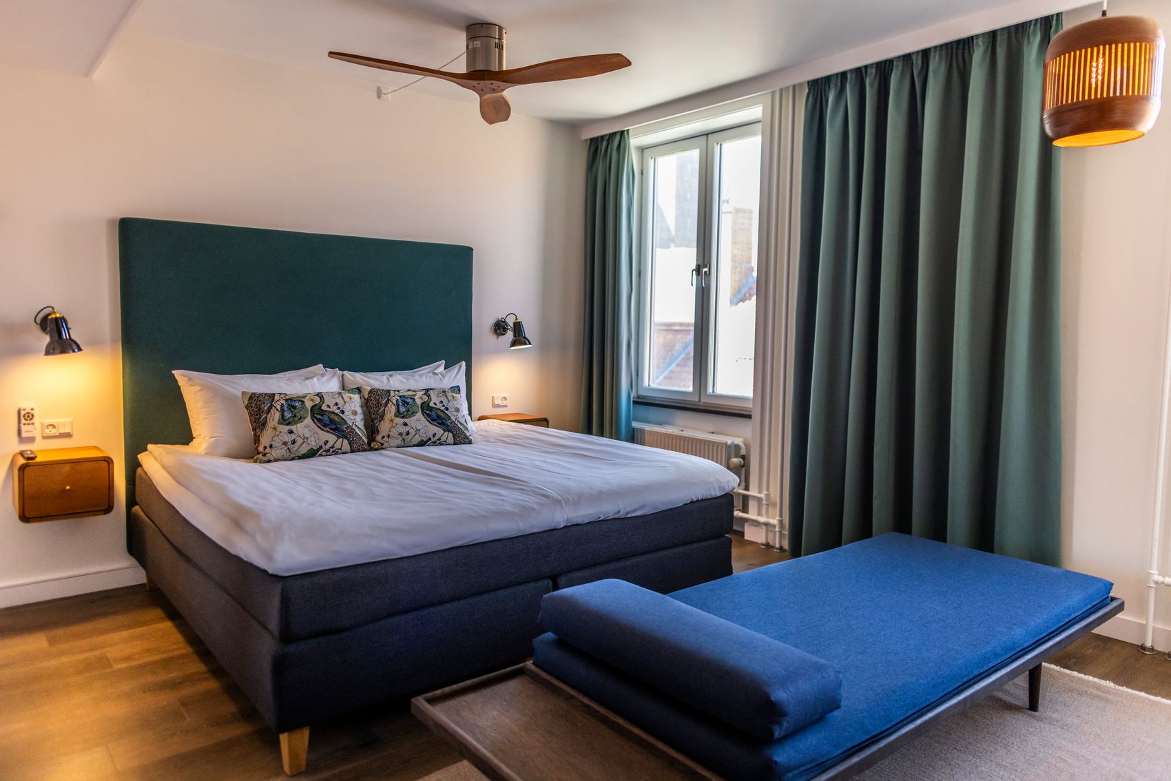 Hotel Motel One Copenhagen Modernes Hotelzimmer mit großem, komfortablem Doppelbett, weichen Kissen, großen Fenstern und ruhiger Atmosphäre durch gedämpfte Beleuchtung und dekorative Vorhänge.