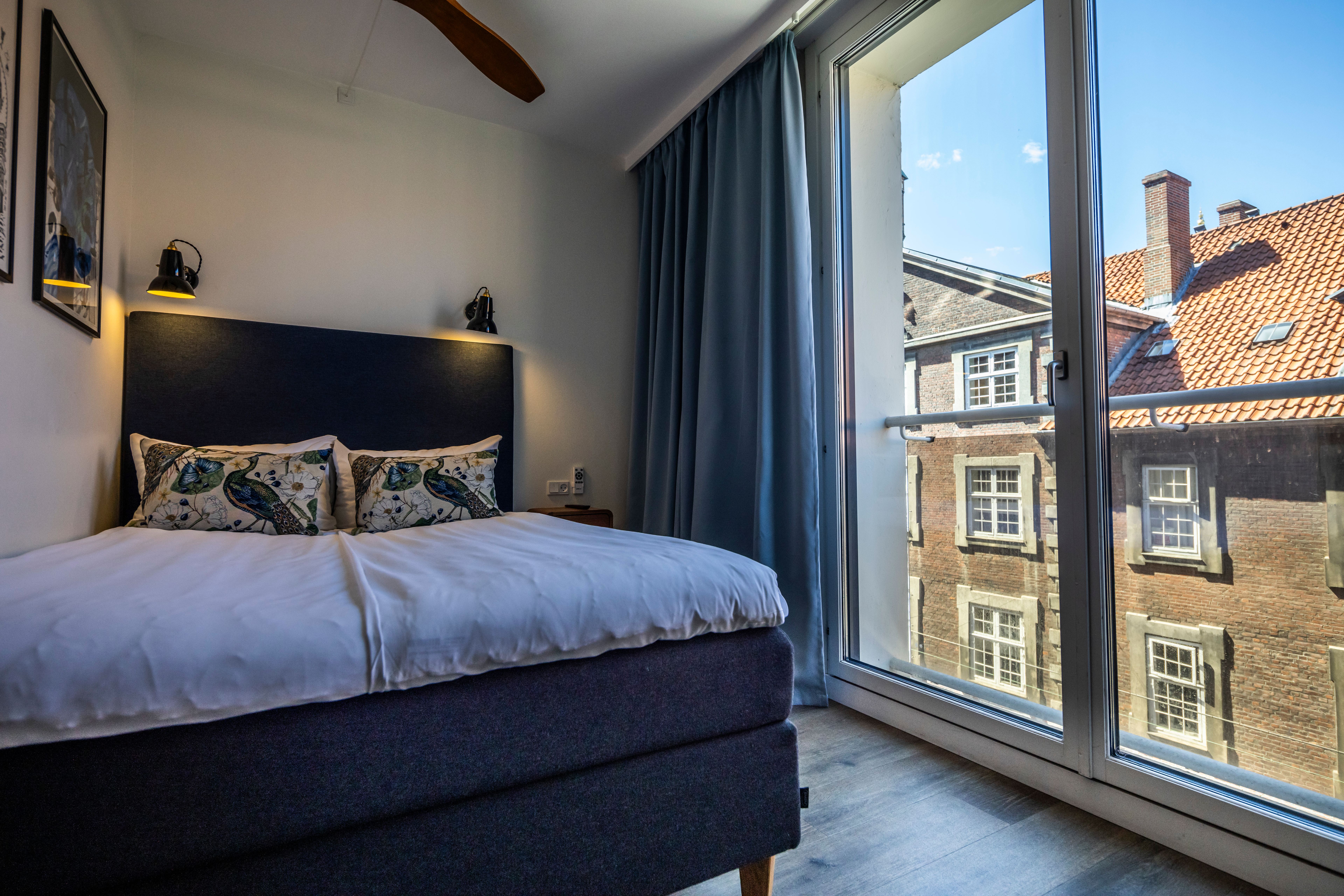 Hotel Motel One Copenhagen Gemütliches Doppelzimmer mit großem Bett, stilvollen Kissen und direktem Blick auf historische Gebäude durch raumhohe Fenster, die viel Tageslicht ins Zimmer lassen. Hotel Motel One Copenhagen Gemütliches Doppelzimmer mit großem Bett, stilvollen Kissen und direktem Blick auf historische Gebäude durch raumhohe Fenster, die viel Tageslicht ins Zimmer lassen.