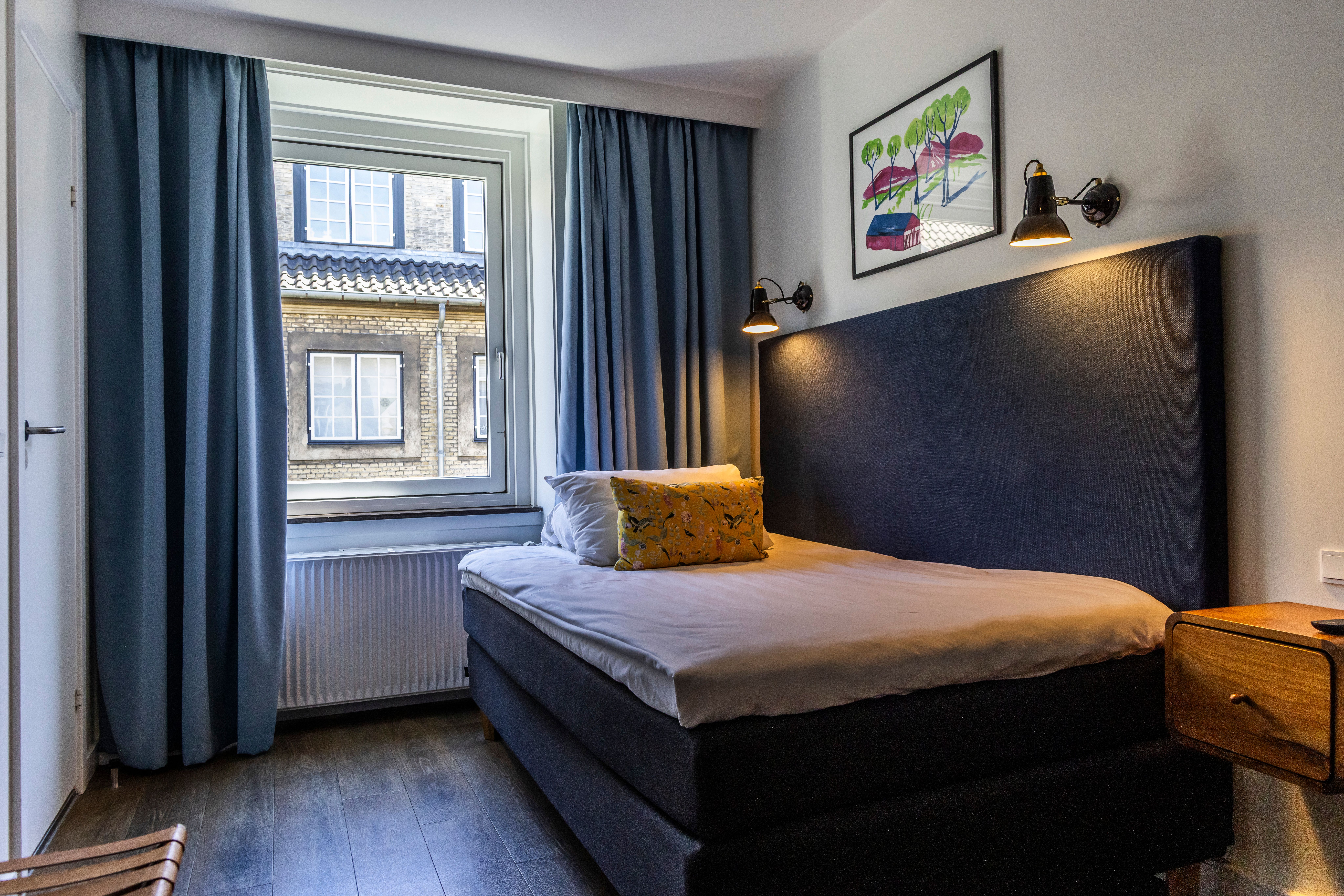 Hotel Motel One Copenhagen Kompaktes Hotelzimmer mit Einzelbett, großem Fenster, gedämpfter Beleuchtung und schlichter Dekoration für eine ruhige und angenehme Unterkunft.