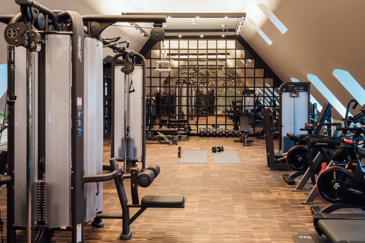 Heller, moderner Fitnessraum mit Kraft- und Ausdauergeräten, zwei Yogamatten auf Holzfußboden und großem Spiegelwand, ideal für effektives Training und Fitness im Hotel.