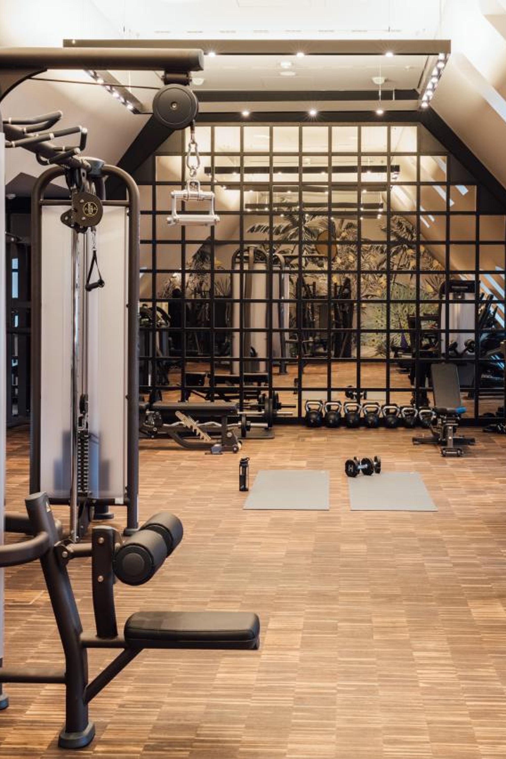 Heller, moderner Fitnessraum mit Kraft- und Ausdauergeräten, zwei Yogamatten auf Holzfußboden und großem Spiegelwand, ideal für effektives Training und Fitness im Hotel.