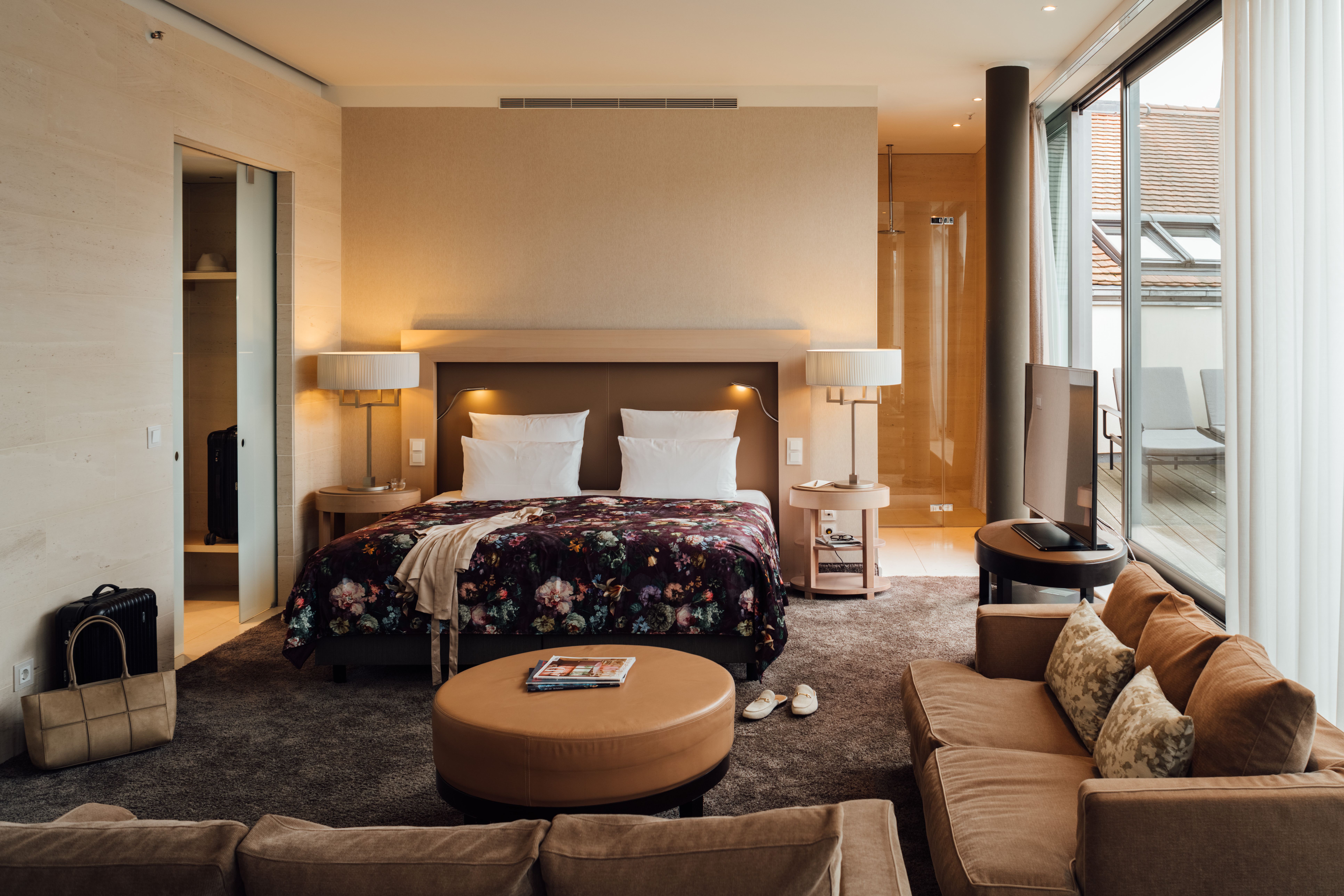 Modern eingerichtetes Hotelzimmer mit großem Doppelbett, gemütlichem Sofa, warmem Licht und Zugang zu einem Balkon mit Außenblick für entspannte Aufenthalte. Modern eingerichtetes Hotelzimmer mit großem Doppelbett, gemütlichem Sofa, warmem Licht und Zugang zu einem Balkon mit Außenblick für entspannte Aufenthalte.