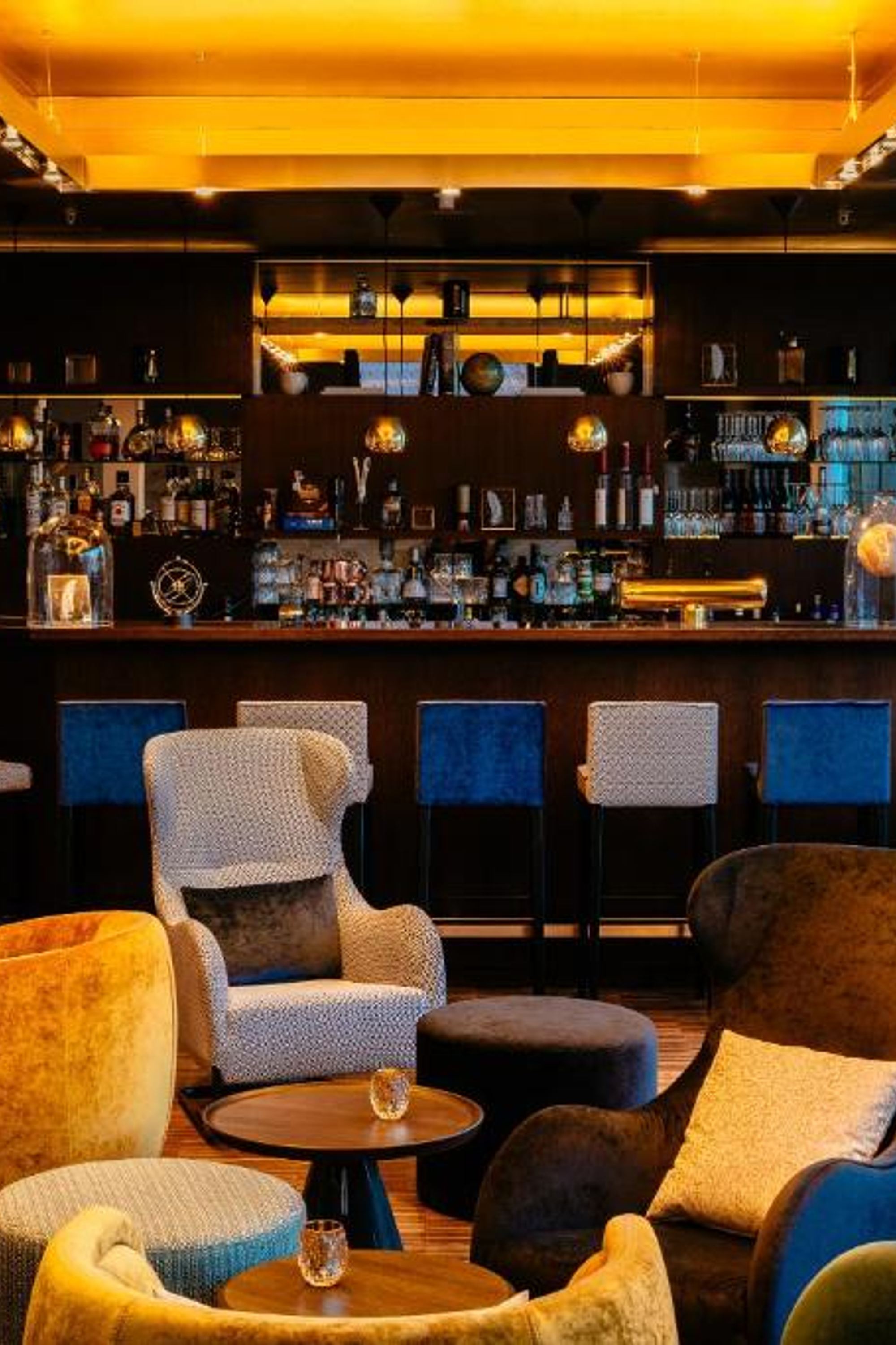 Gemütliche Hotelbar mit warmem Licht, bequemen Sesseln und kleinen Tischen, ideal zum Entspannen und geselligen Beisammensein. Elegante Bar im Hintergrund mit breitem Getränkeangebot.