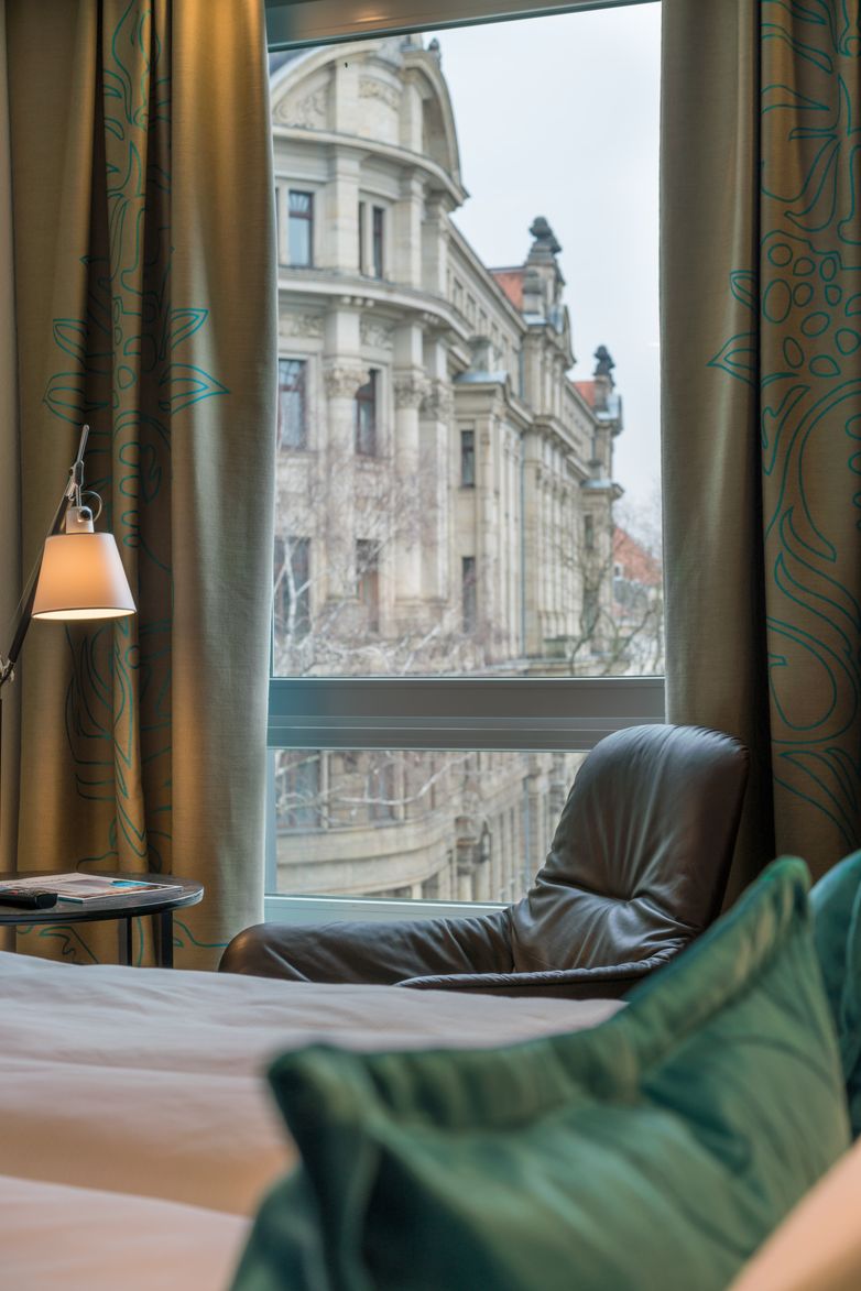 Designhotel Dresden Palaisplatz Motel One Zimmer mit Blick über das Bett hin auf einen Sessel vor bodentiefem Fenster