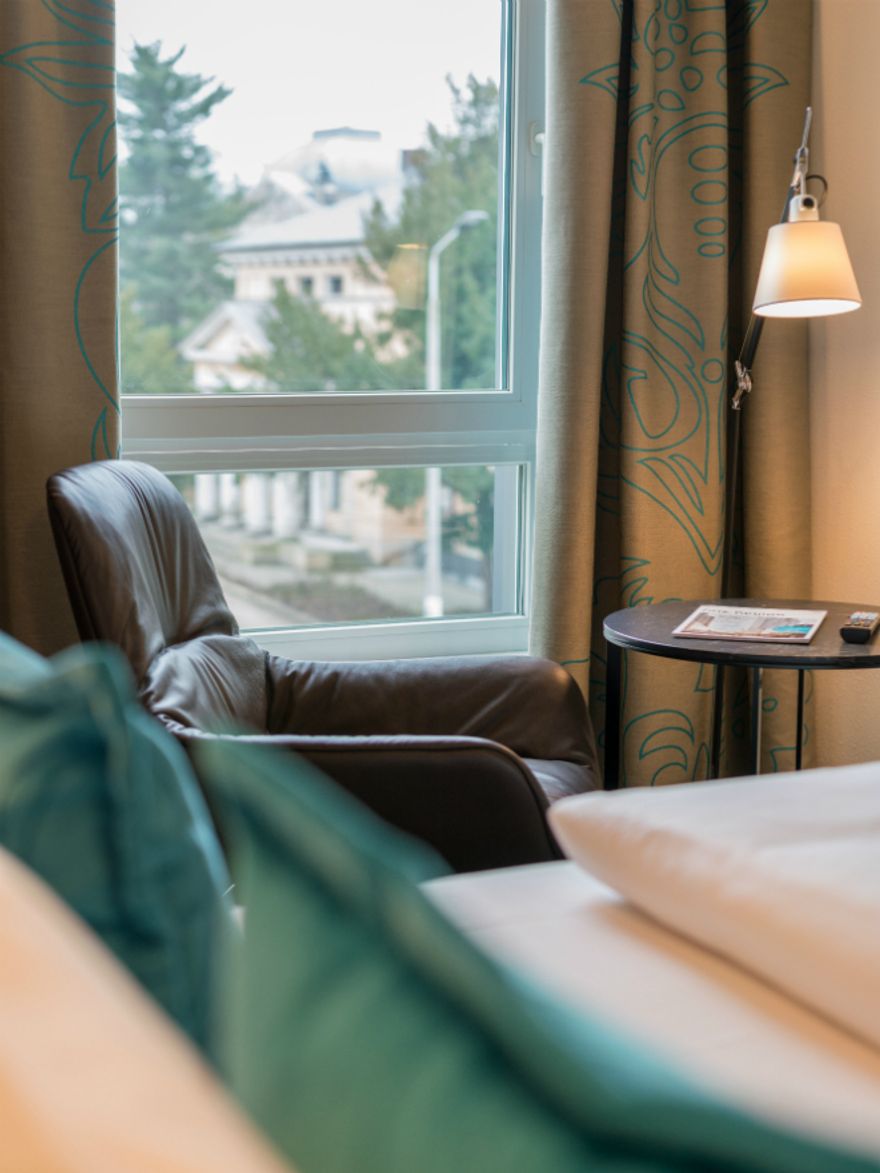 Designhotel Dresden Palaisplatz Motel One seitlicher Blick über ein Bett auf einen Sessel, der vor einem Fenster steht