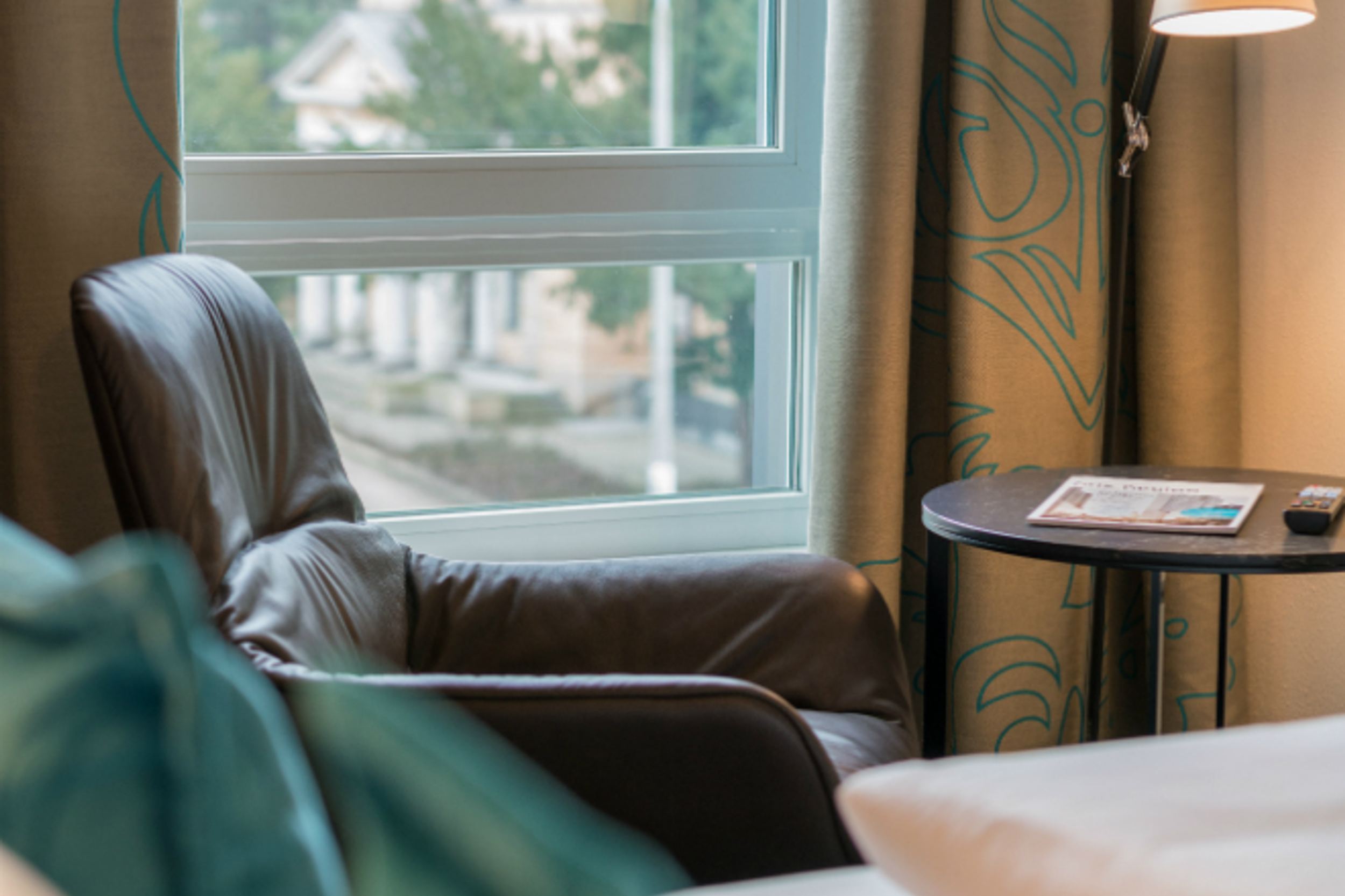 Designhotel Dresden Palaisplatz Motel One seitlicher Blick über ein Bett auf einen Sessel, der vor einem Fenster steht