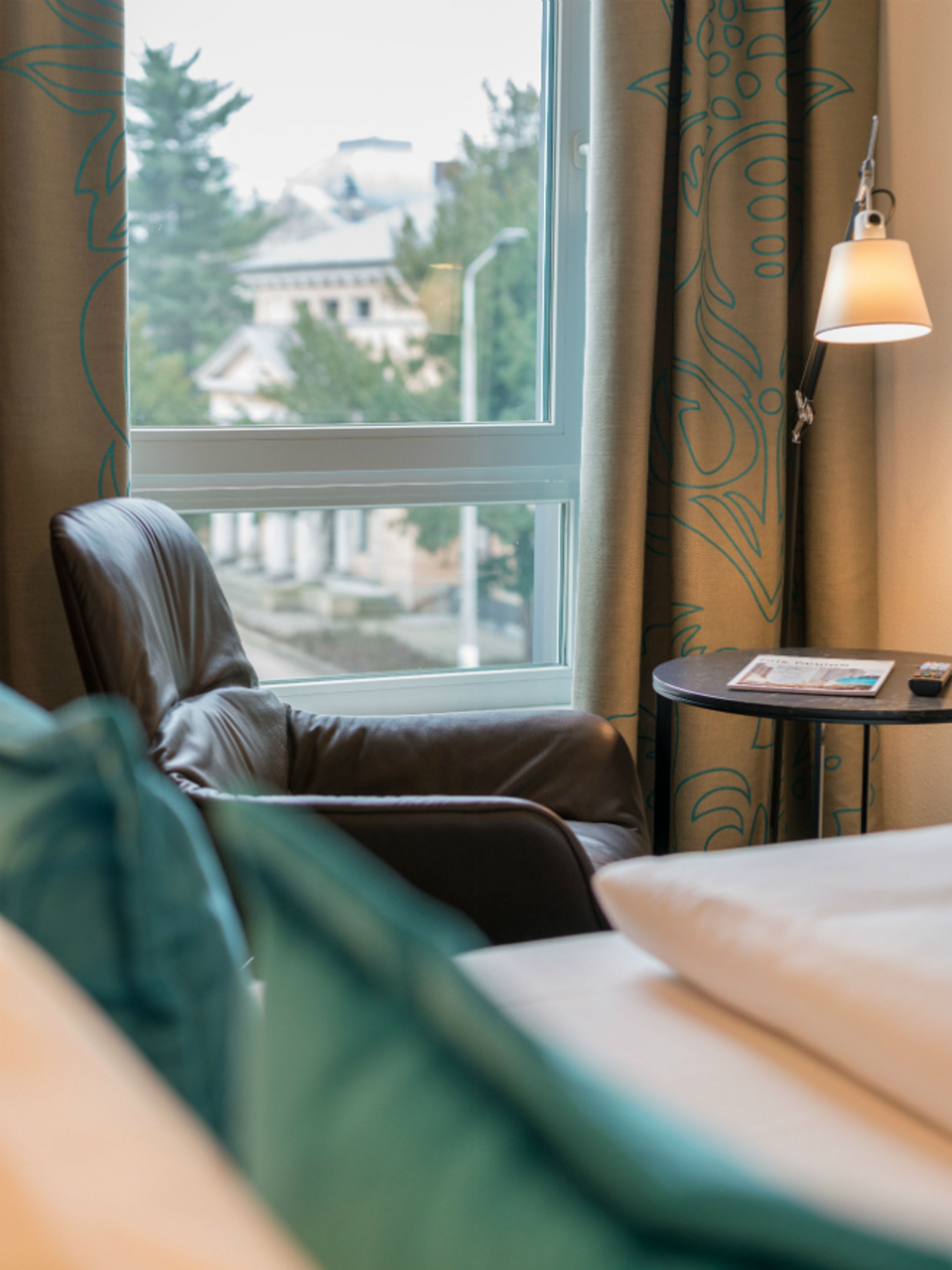 Designhotel Dresden Palaisplatz Motel One seitlicher Blick über ein Bett auf einen Sessel, der vor einem Fenster steht