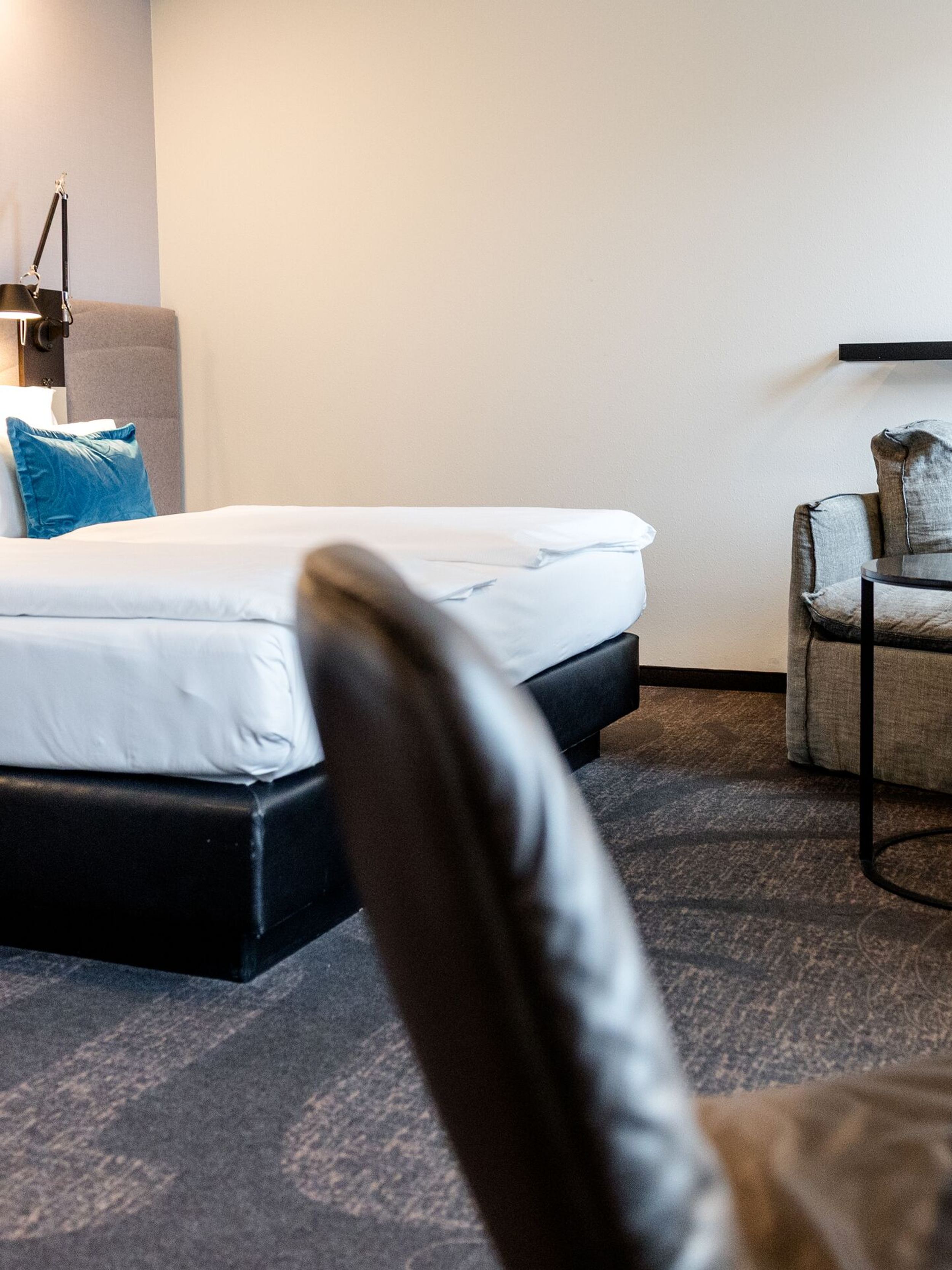 Hotel Motel One Dresden-Palaisplatz Modern eingerichtetes Hotelzimmer mit großem Doppelbett, hellen Wänden, drei blauen Kissen, Sitzbereich mit zwei Sesseln und kleinem runden Tisch, angenehmer, ruhiger Atmosphäre.