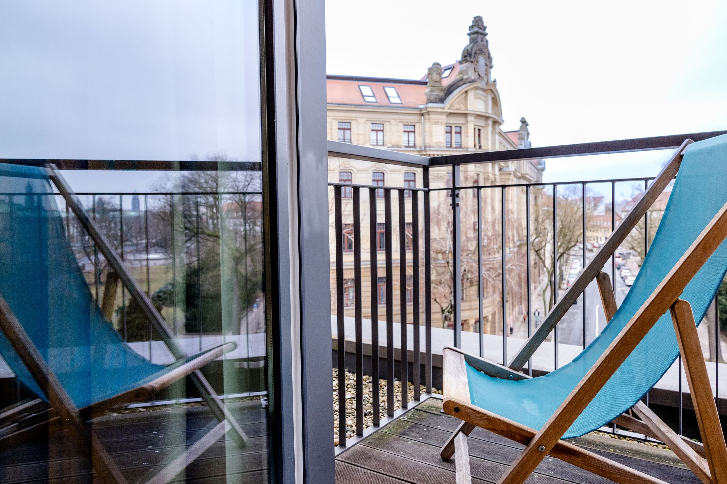 Hotel Motel One Dresden-Palaisplatz Balkon mit zwei blauen Liegestühlen, Blick auf historische Gebäude, ruhige Atmosphäre, ideal zum Entspannen und Stadtblick genießen.