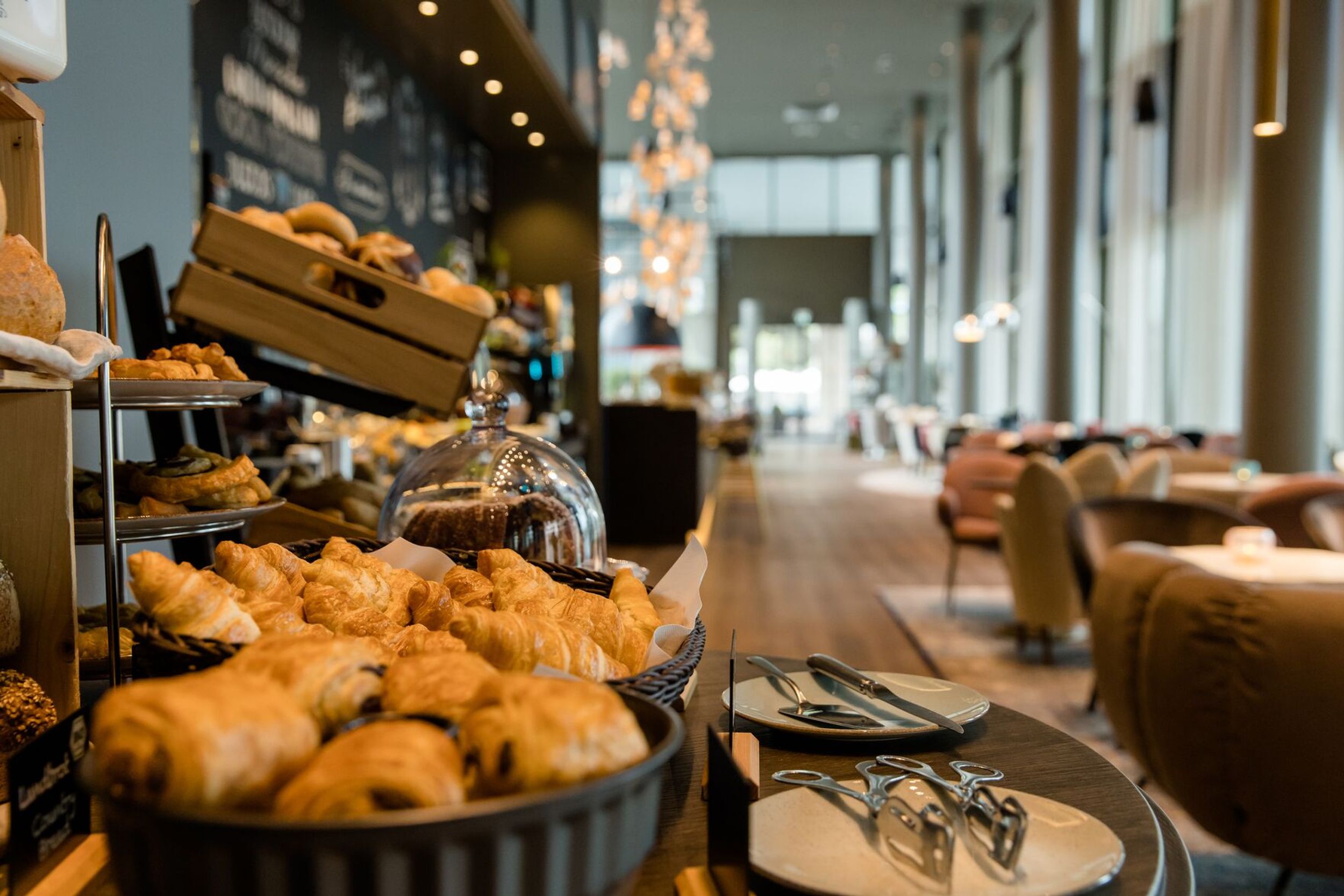 Hotel Dresden am Zwinger Motel One heller Frühstücksraum mit Sitzgelegenheiten sowie Fokus auf Backwaren im Vordergrund