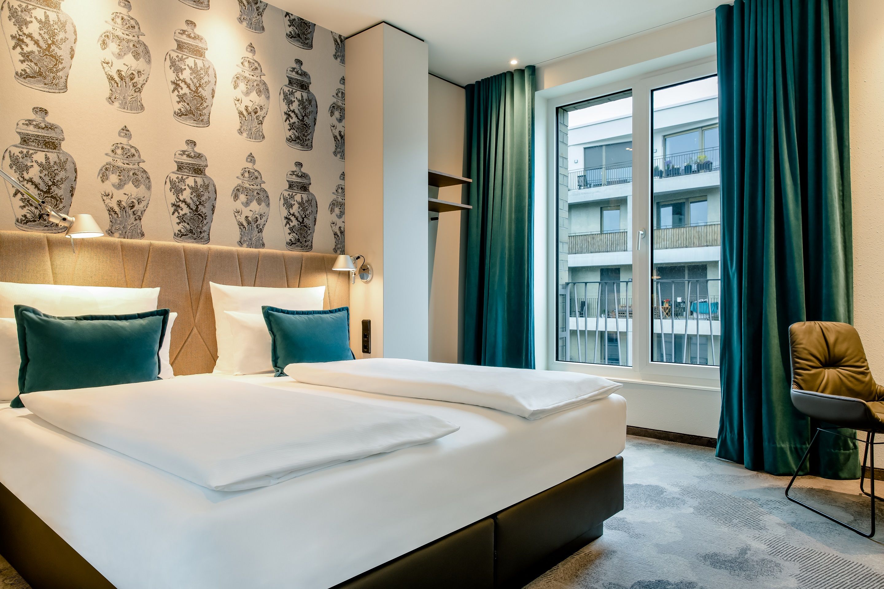 Designhotel Dresden am Zwinger Motel One geräumiges Zimmer mit Doppelbett, Sessel, offenen Schrankregalen sowie bodentiefen Fenstern
