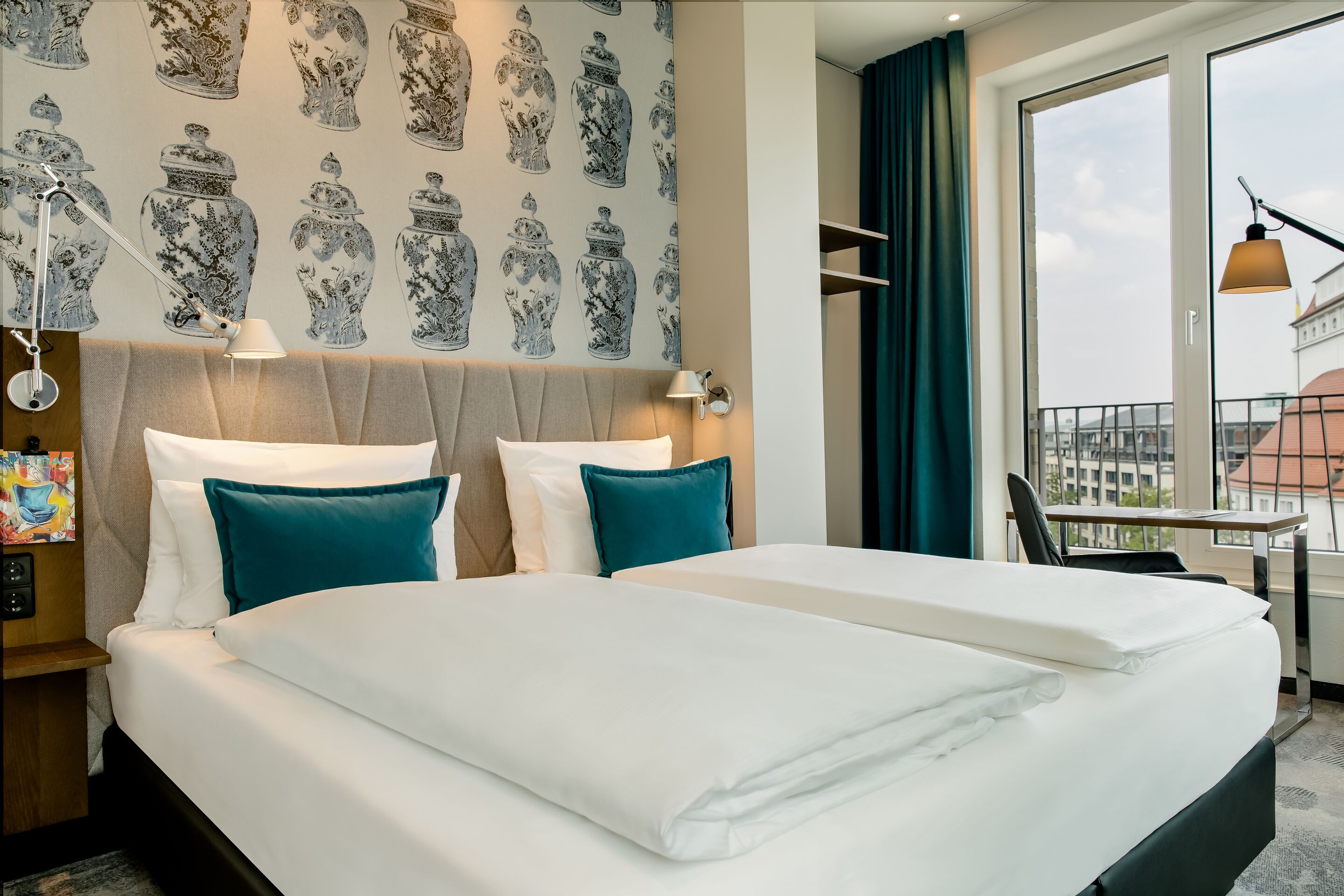 Hotel Motel One Dresden am Zwinger Modern eingerichtetes Hotelzimmer mit großem Doppelbett, weißen Bettdecken und türkisfarbenen Kissen. Große Fenster bieten Stadtblick, ein Schreibtisch und dezente Wanddekoration schaffen eine einladende Atmosphäre. Hotel Motel One Dresden am Zwinger Modern eingerichtetes Hotelzimmer mit großem Doppelbett, weißen Bettdecken und türkisfarbenen Kissen. Große Fenster bieten Stadtblick, ein Schreibtisch und dezente Wanddekoration schaffen eine einladende Atmosphäre.