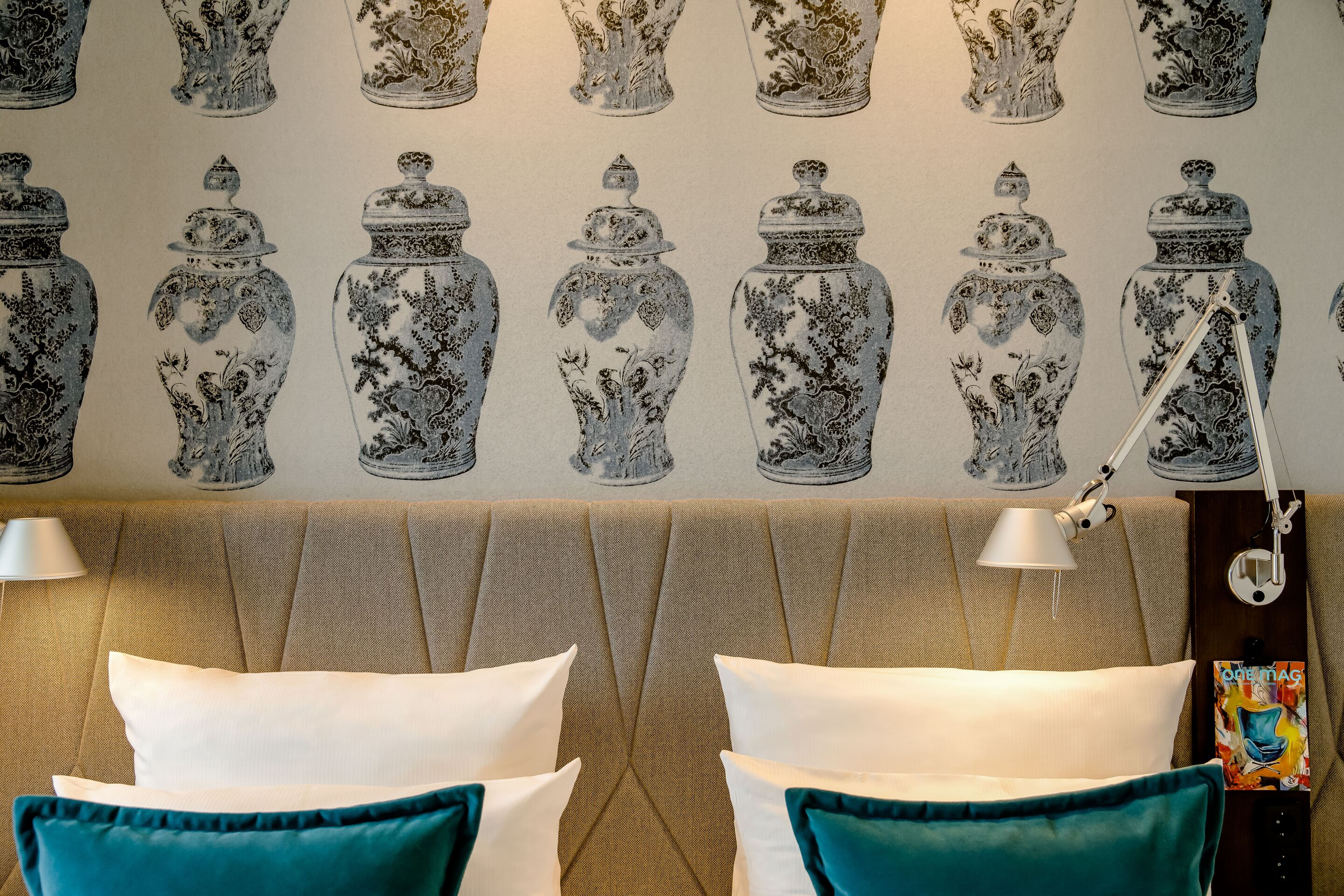 Hotel Motel One Dresden am Zwinger Beidseitiges Doppelbett mit weißen Kissen und türkisfarbenen Zierkissen vor gepolsterter Rückwand. Wand mit dekorativem Tapetenmuster aus schwarz-weißen Vasenmotiven. Zwei verstellbare Leselampen an der Wand. Stimmungsvoll und modern eingerichtet. Hotel Motel One Dresden am Zwinger Beidseitiges Doppelbett mit weißen Kissen und türkisfarbenen Zierkissen vor gepolsterter Rückwand. Wand mit dekorativem Tapetenmuster aus schwarz-weißen Vasenmotiven. Zwei verstellbare Leselampen an der Wand. Stimmungsvoll und modern eingerichtet.