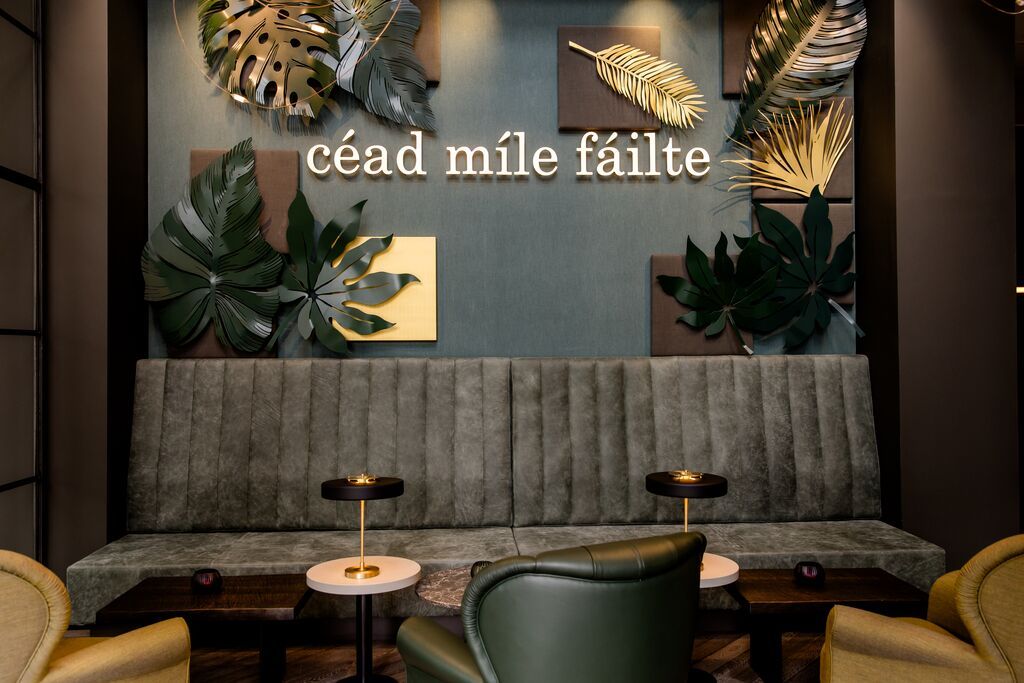 Hotel Dublin Motel One Lounge mit Sitzgelegenheiten und Schriftzug sowie große Blätter als Dekoration an der Wand