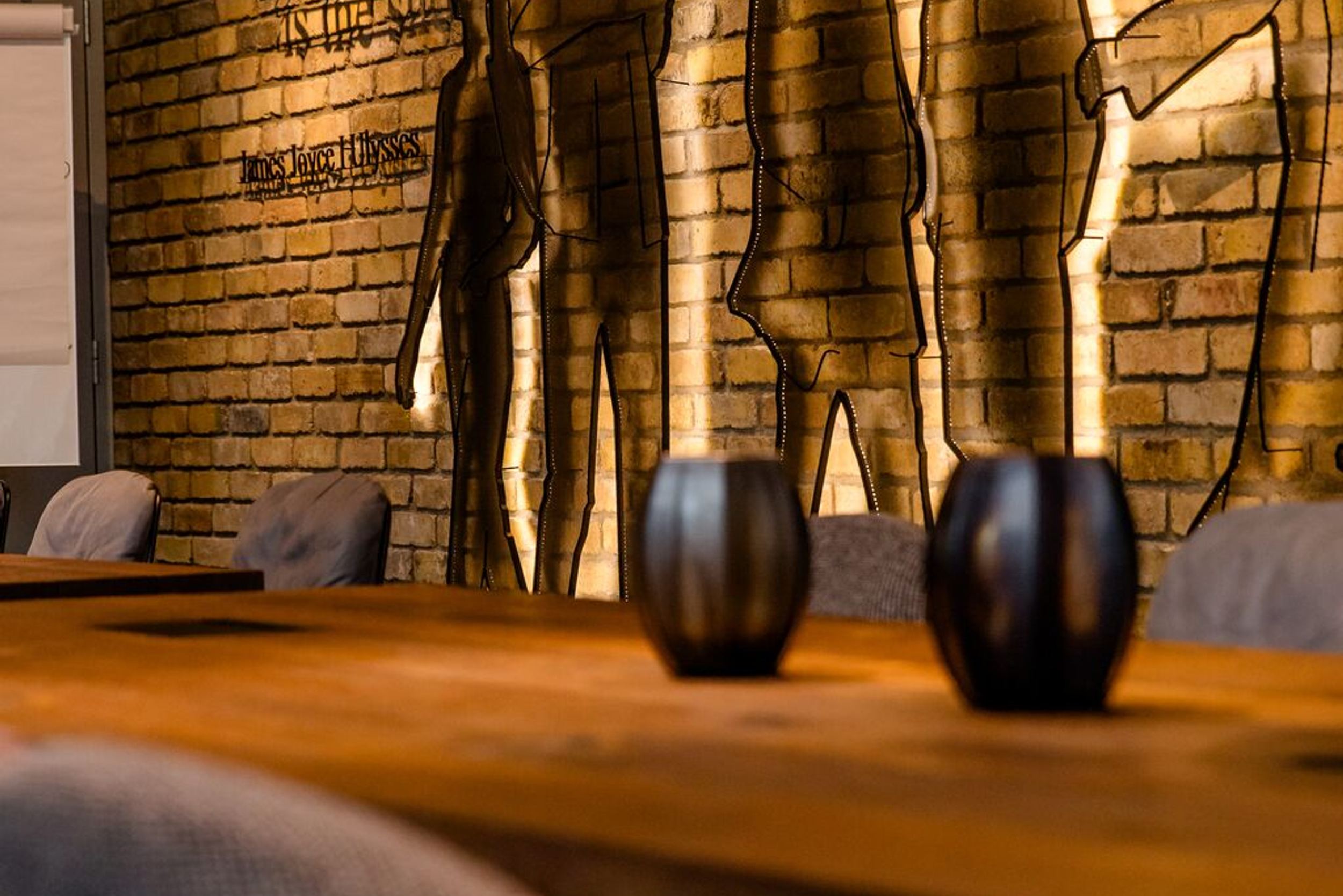 Hotel Dublin Motel One langer Tisch mit Stühlen vor Wandinstallation mit Umrissen von Personen sowie einem Zitat von James Joyce