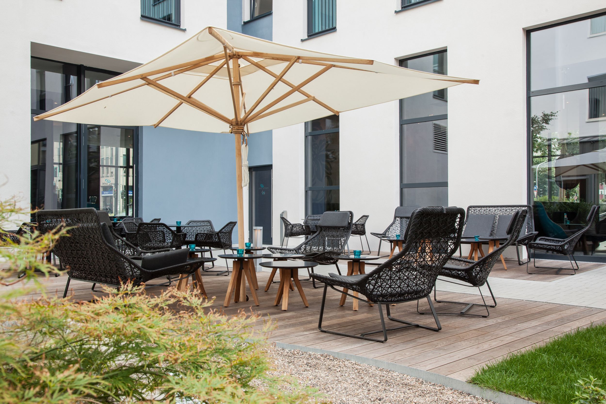 Hotel Düsseldorf Hauptbahnhof Motel One Außenbereich mit Sitzgelegenheiten und hellem Sonnenschirm