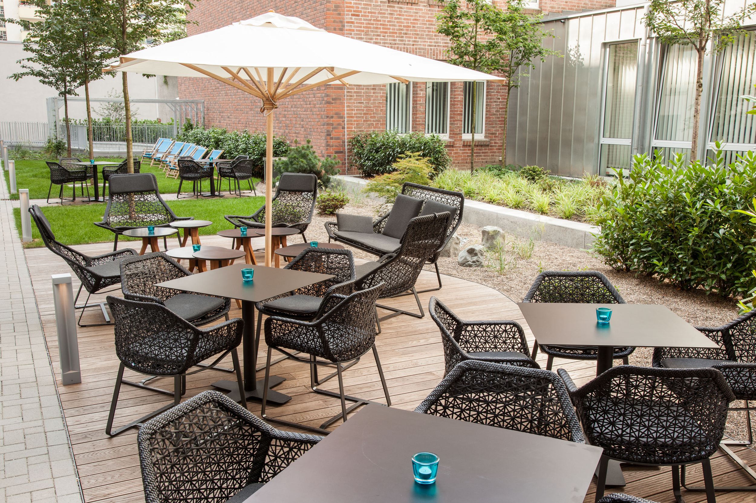 Hotel Düsseldorf Hauptbahnhof Motel One Terrasse mit mehreren Tischen und Stühlen sowie Liegestühle im Hintergrund